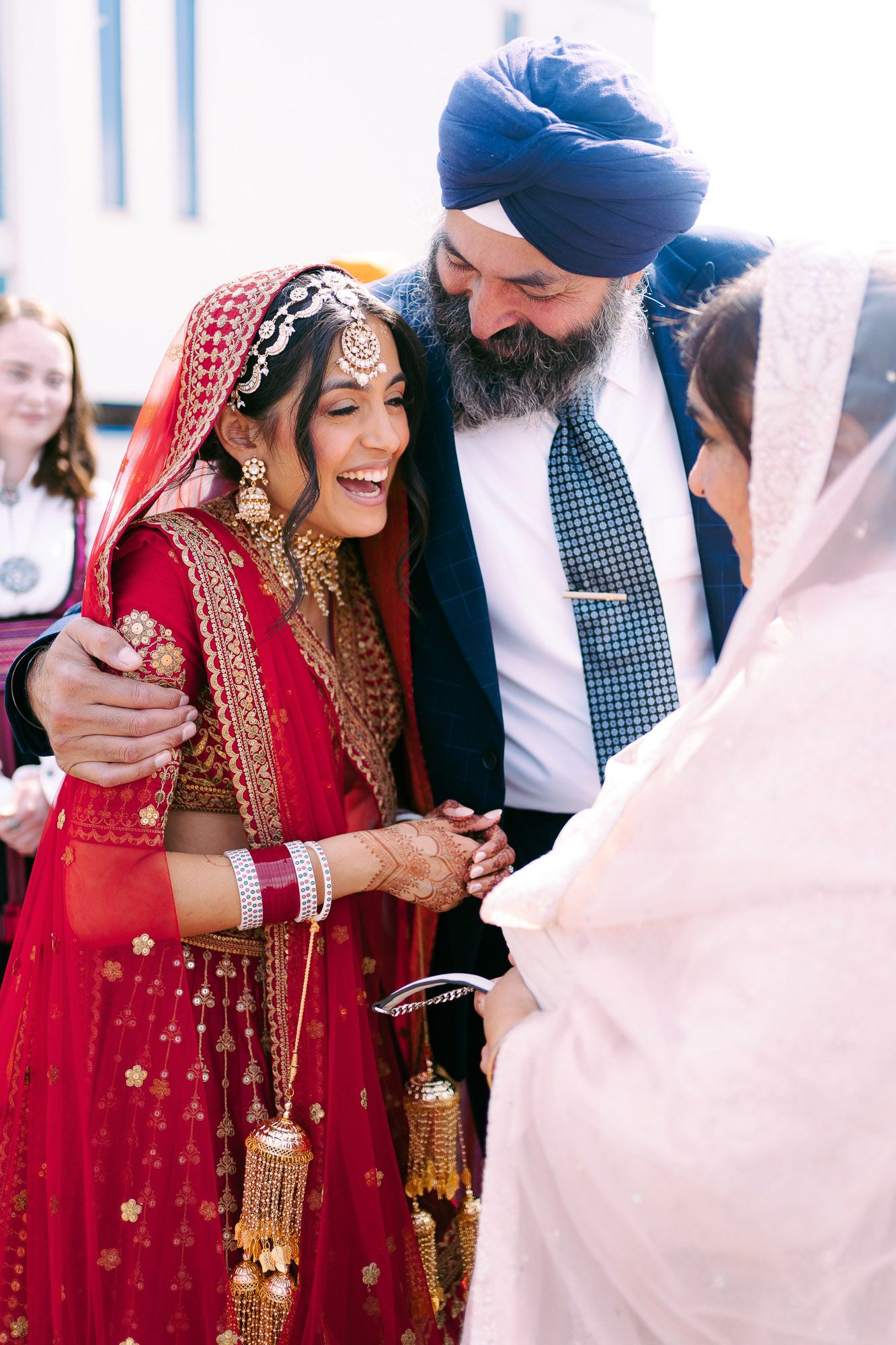A couple shares joyful moments during a traditional Indian wedding ceremony wearing red and navy attire.