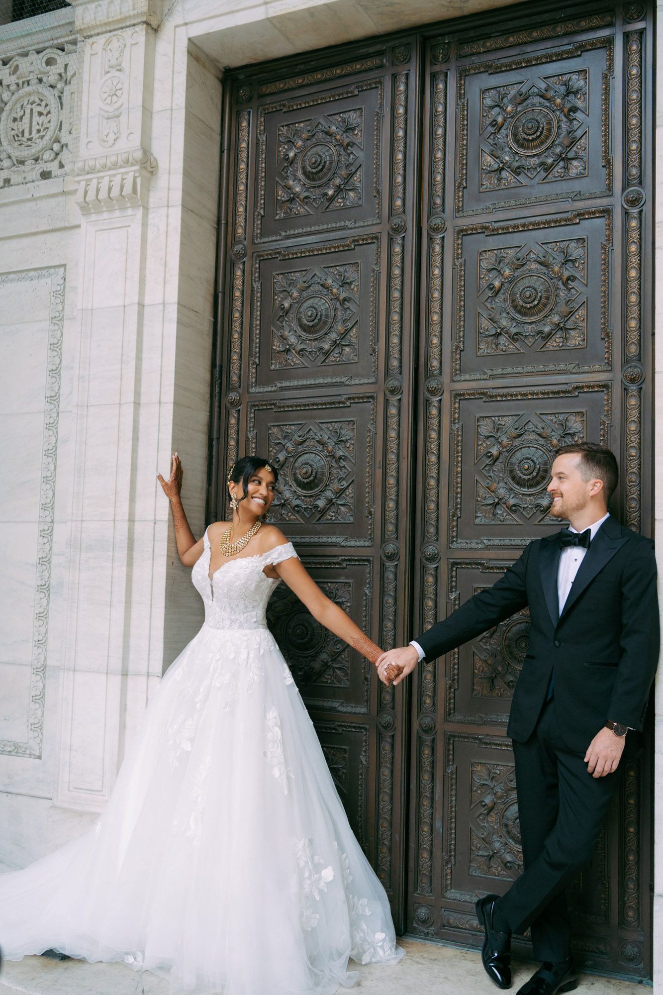Three sequential photos show a couple in wedding attire playfully posing against ornate vintage doors at their wedding venue.
