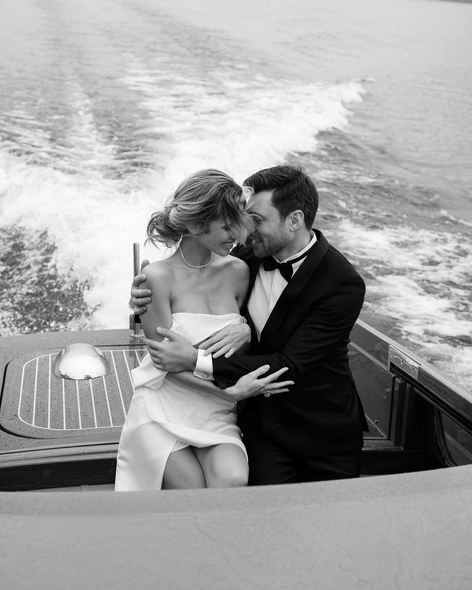 A romantic black and white photo of a couple embracing on a boat, with ocean waves trailing behind them. wedding photographer Italy, Como,