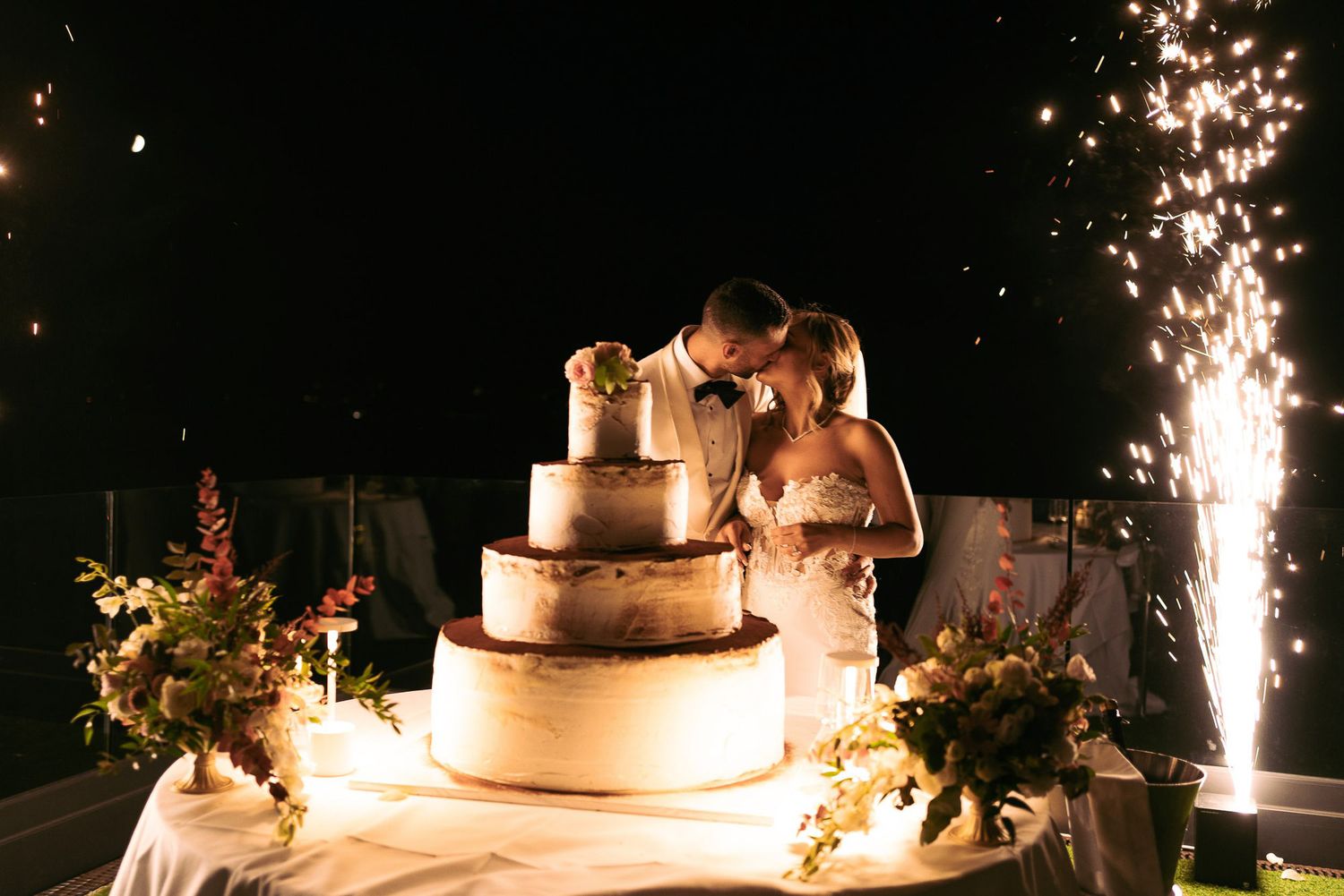 A wedding cake decorated with sparklers creating a magical glowing effect against a dark background.
