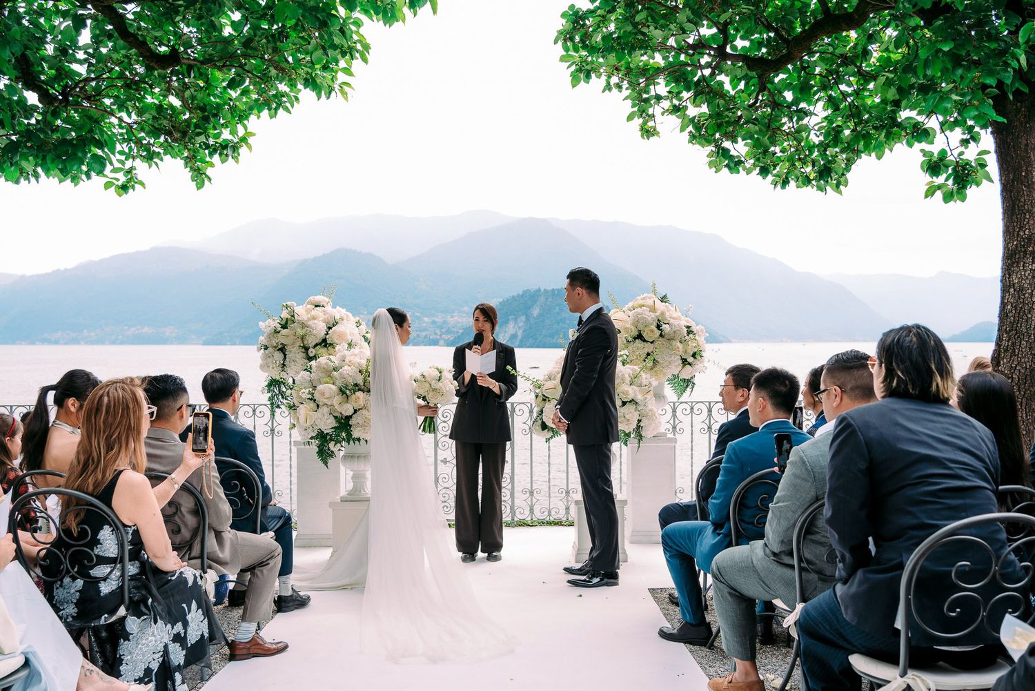 Wedding guests gather for an outdoor ceremony overlooking a scenic mountain landscape with lush greenery.