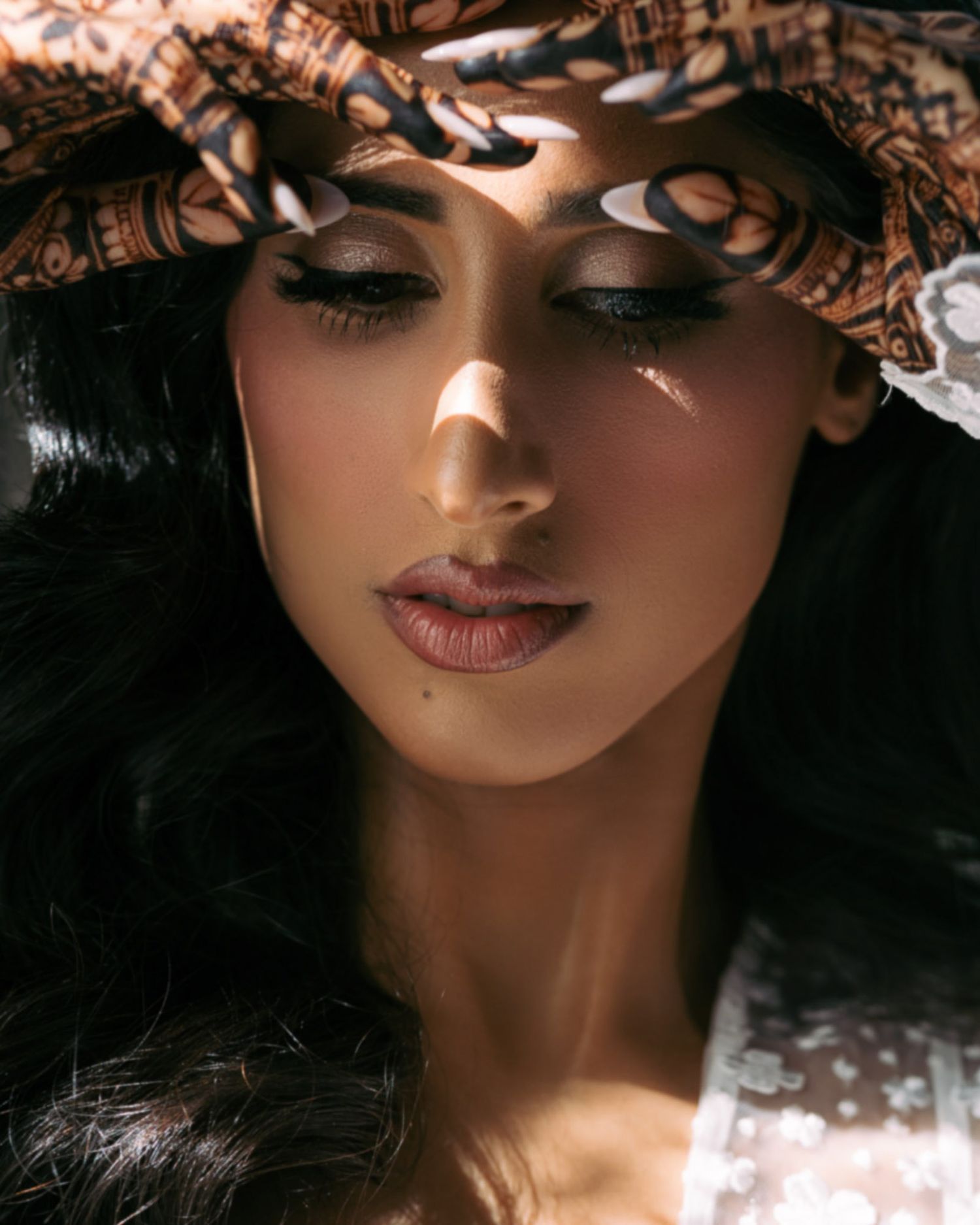 Close up beauty portrait showing dramatic eye makeup and glossy lips in moody lighting.
