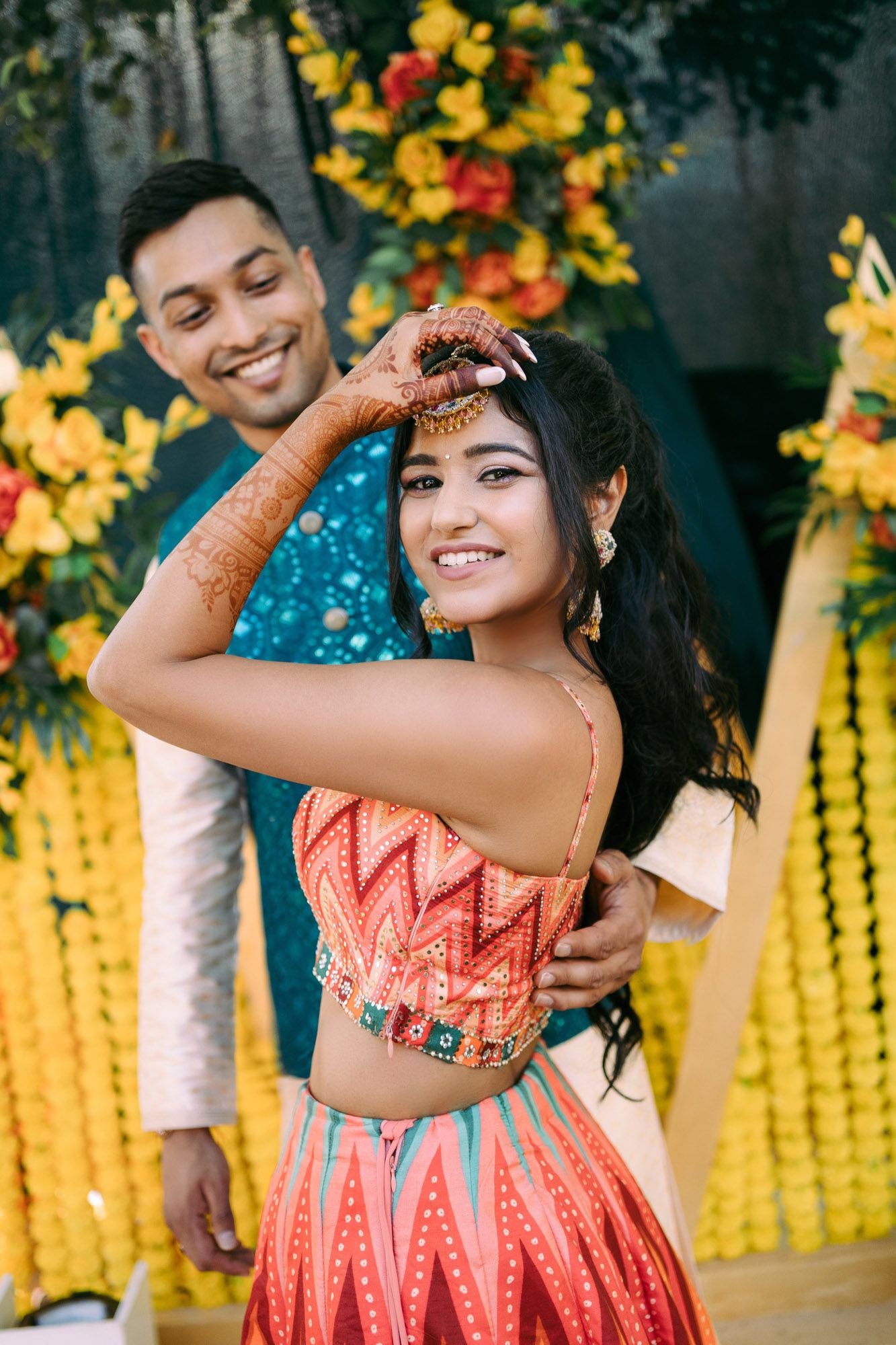 A couple poses playfully in front of yellow floral decorations during a festive celebration.