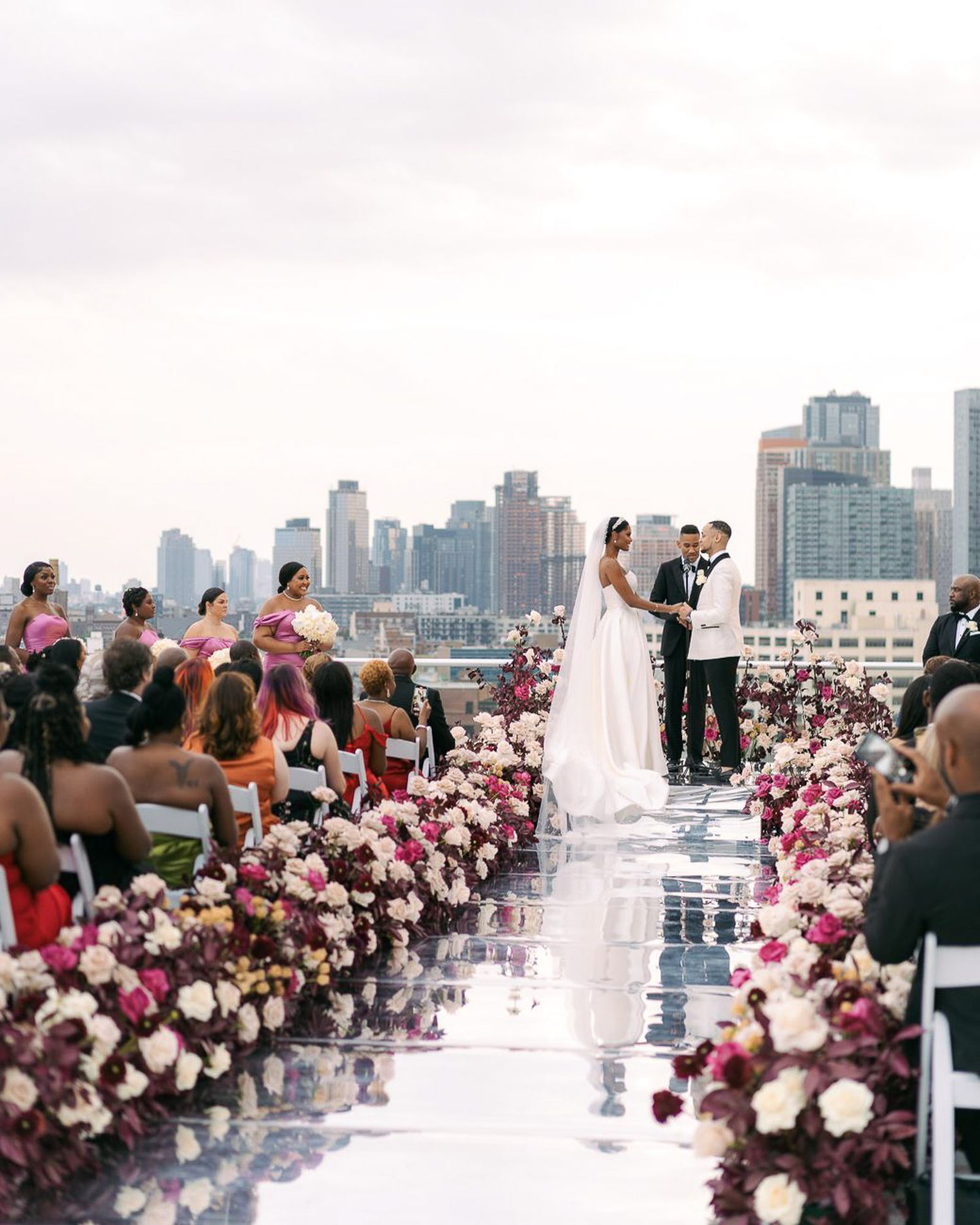 A panoramic rooftop wedding ceremony setup with pink and white floral arrangements and city skyline backdrop.