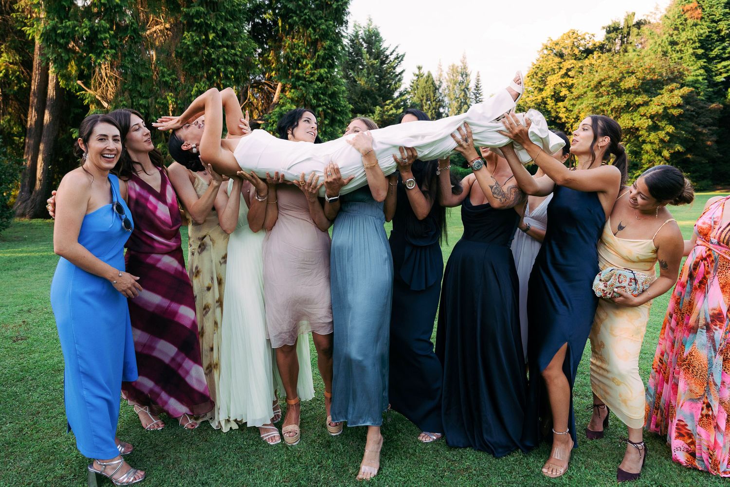 Wedding party members laugh and pose together outdoors in colorful formal attire during summer celebration.