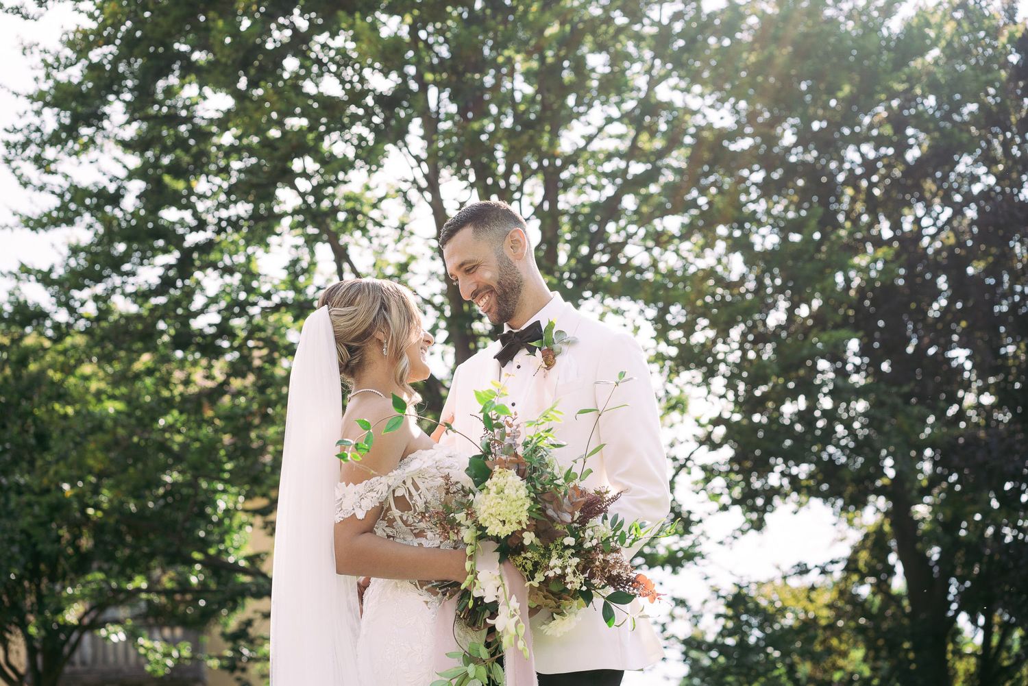 A romantic outdoor wedding scene in a lush garden setting with soft natural lighting and white floral decorations.