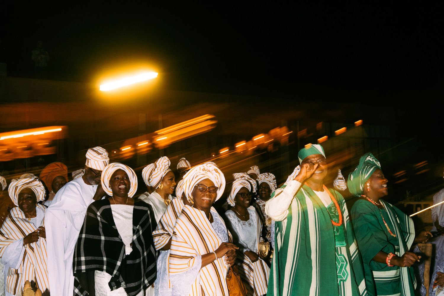 People in traditional white and green robes gather outdoors during a nighttime ceremony.