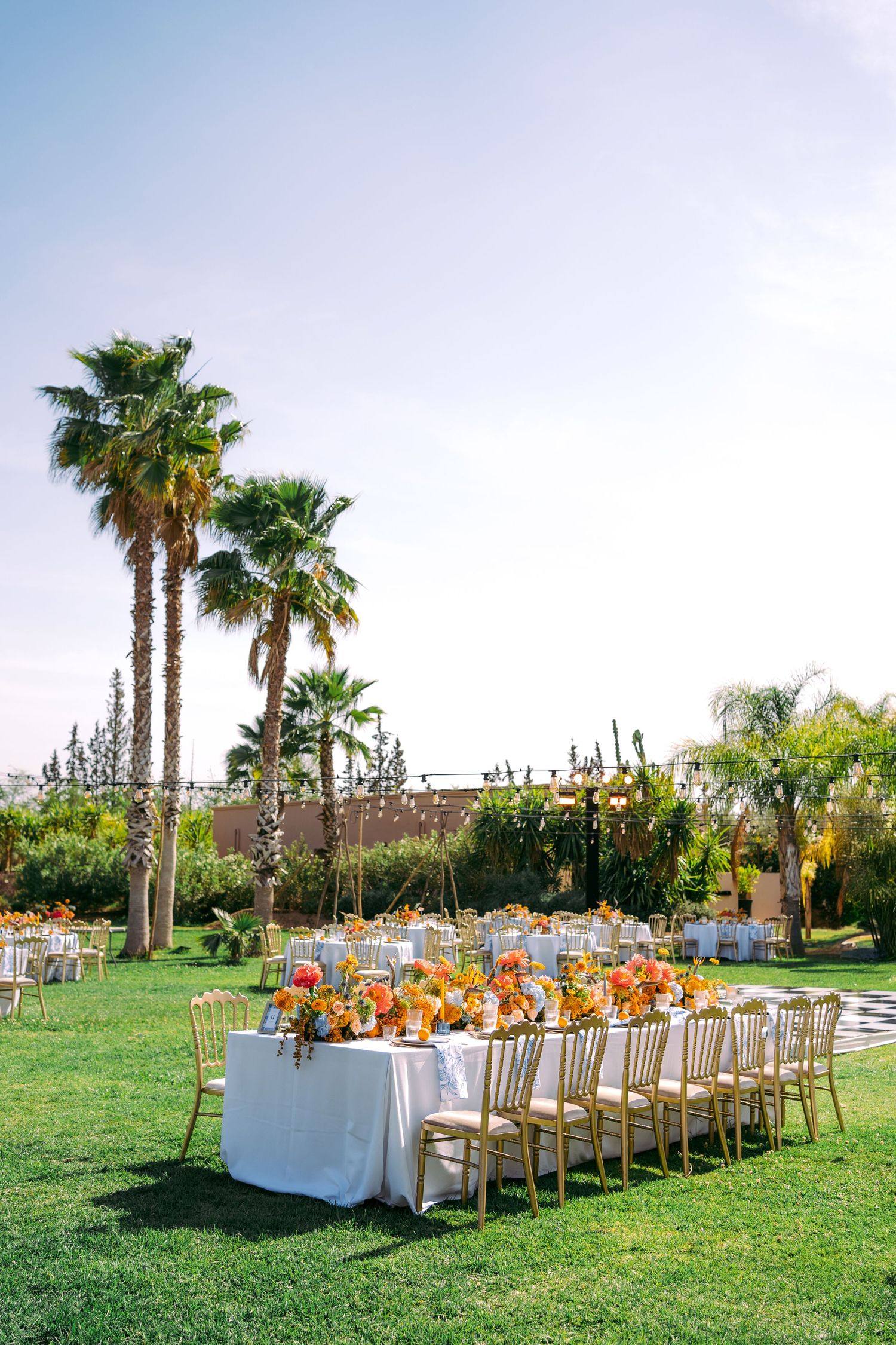 Elegant outdoor wedding reception setup with white tables and chairs surrounded by palm trees.