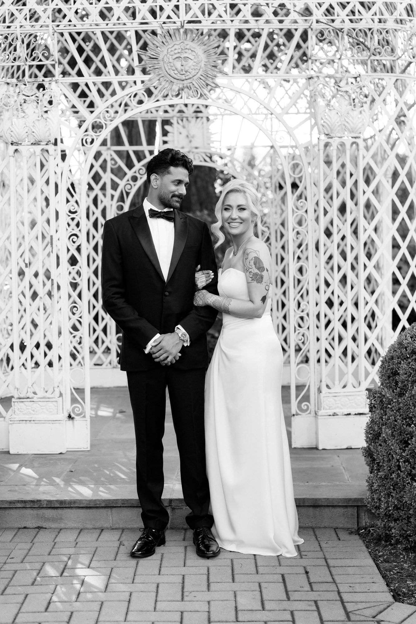 Wedding couple shares a joyful moment together on a paved terrace with decorative white lattice backdrop.