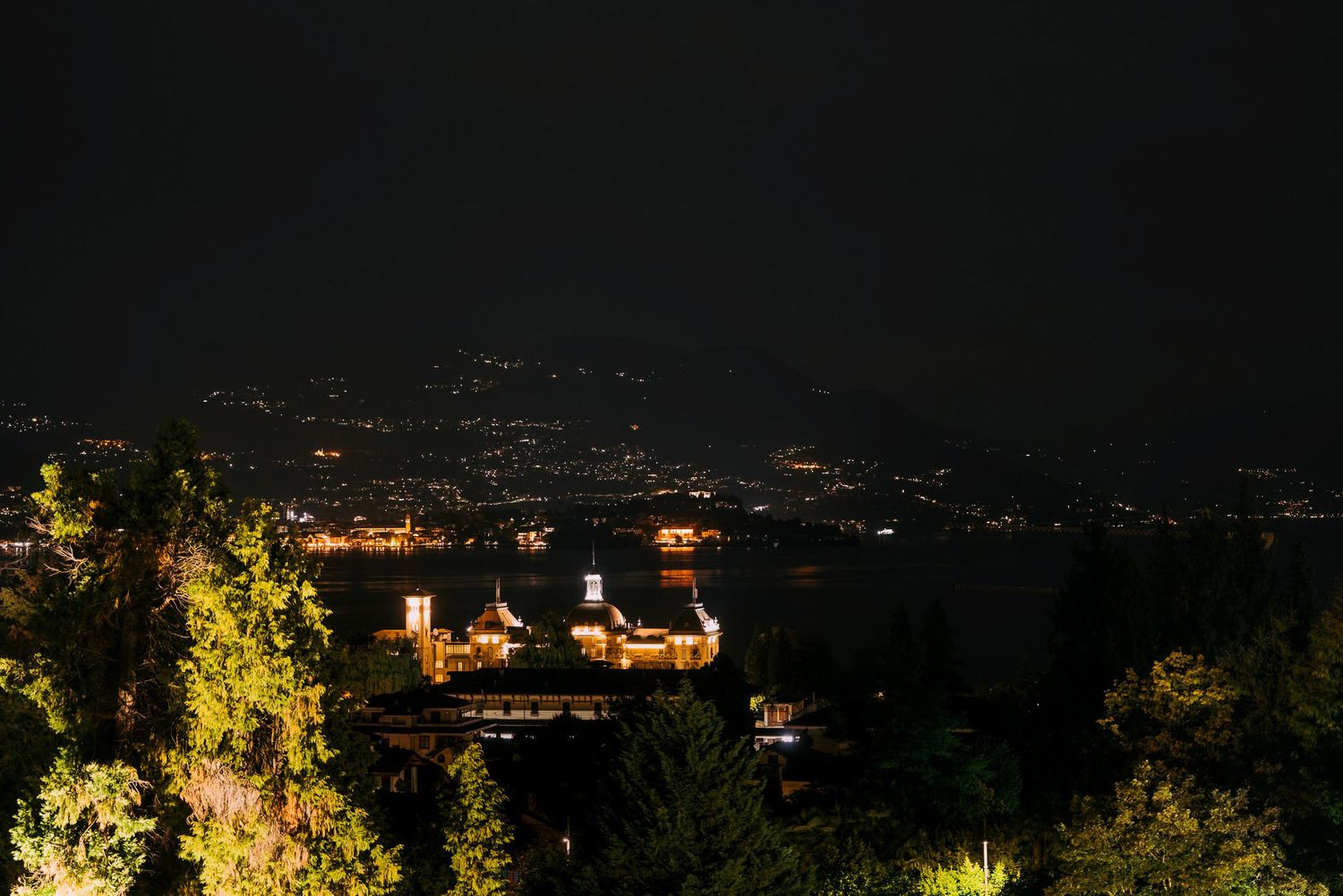 Panoramic aerial view of city lights illuminating a dark mountainous landscape at night.