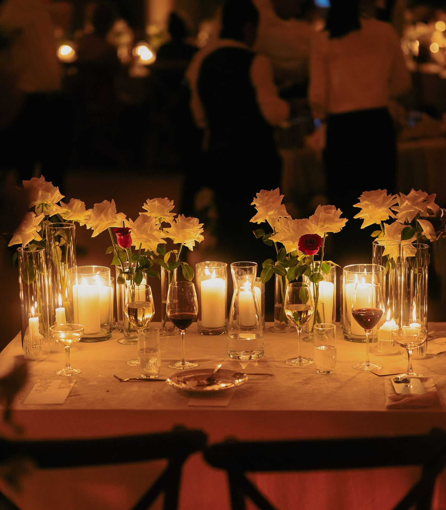 Elegant table setting with glowing candles and white flowers in glass vases creating a romantic ambiance at evening event.