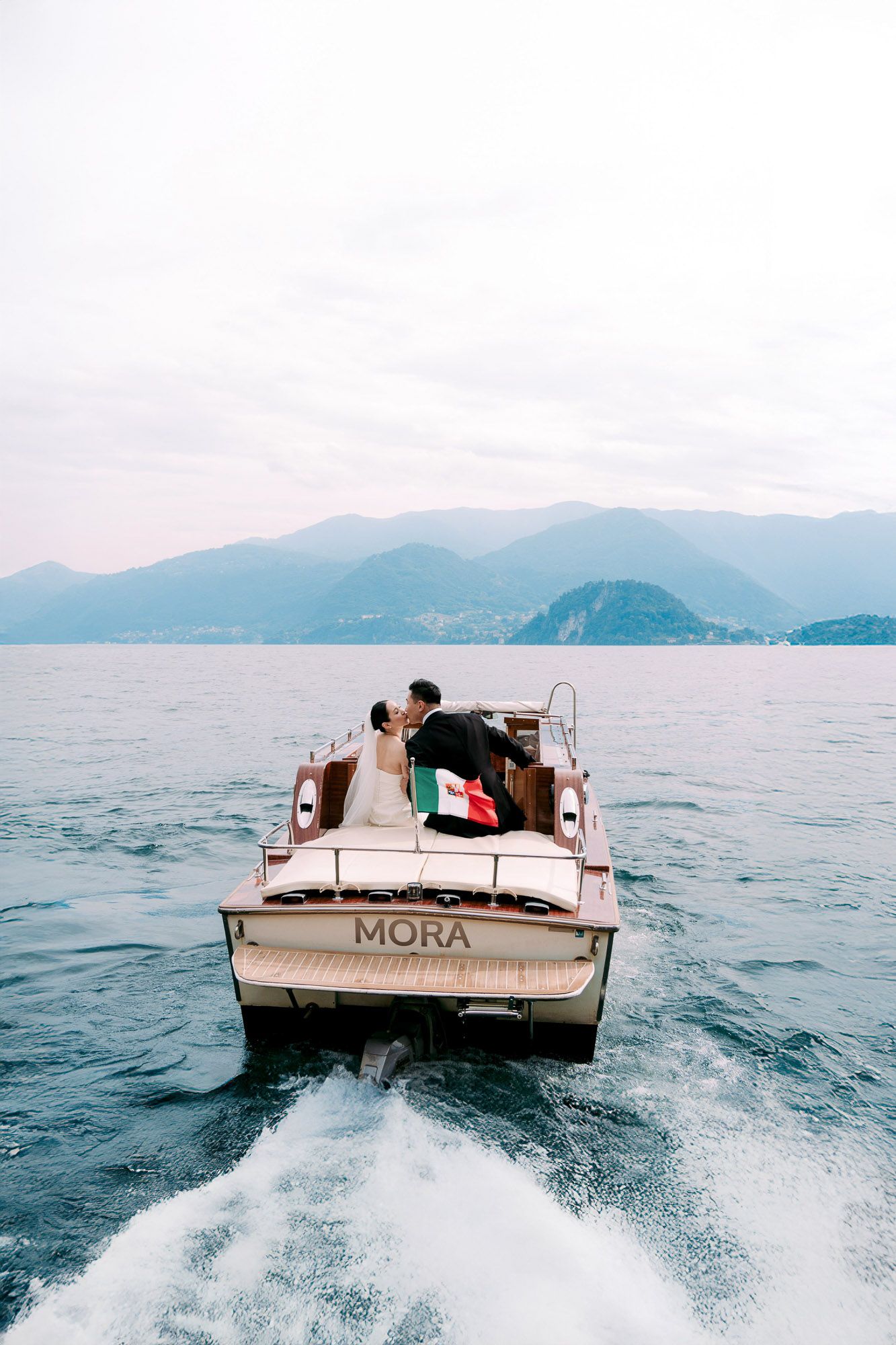 A boat speeds across Lake Como with mountains in the background creating a wake on the blue waters.