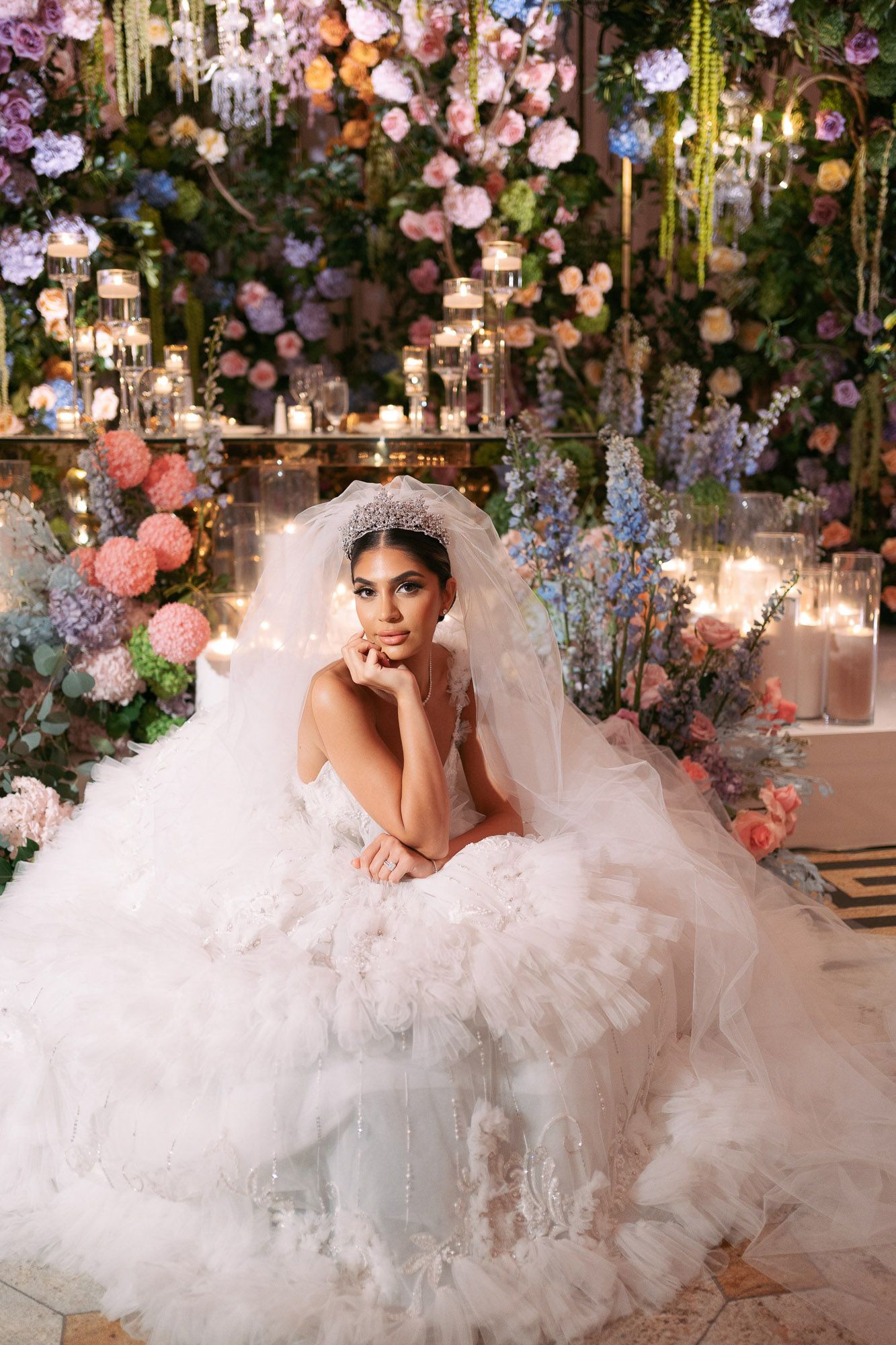 Ethereal bridal photoshoot featuring a flowing white tulle gown amidst a romantic floral garden backdrop with hanging lights.
