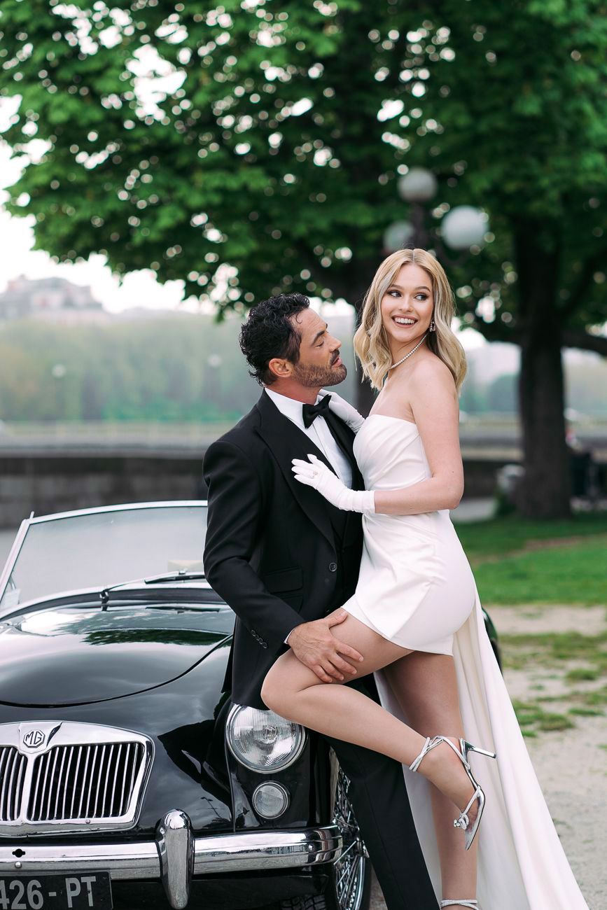 A couple poses playfully in front of a vintage black car during a romantic photoshoot. wedding photographer Italy, Como, France