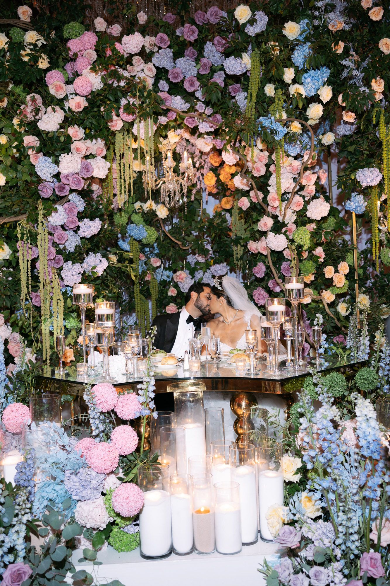 Romantic wedding reception decor with hanging pastel flowers, greenery and glass lanterns creating an enchanted garden ceiling.