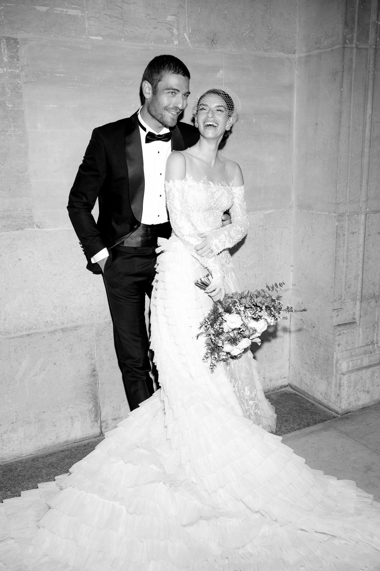 A black and white wedding photo series showing a couple laughing and embracing against a stone wall.
