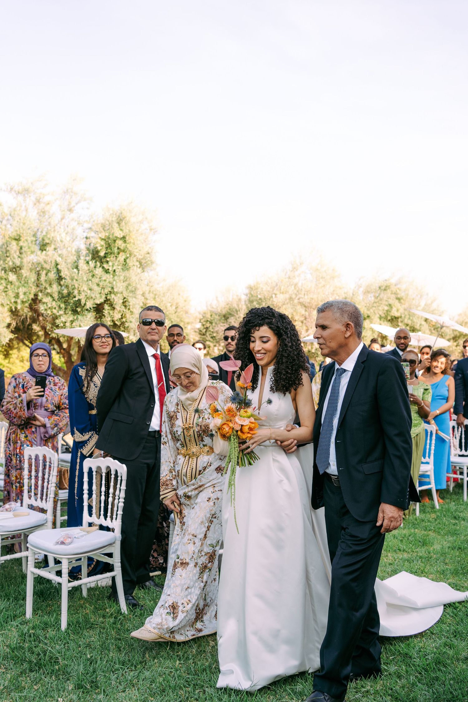 Wedding ceremony guests gathering on a sunny lawn with white chairs set up for the celebration.