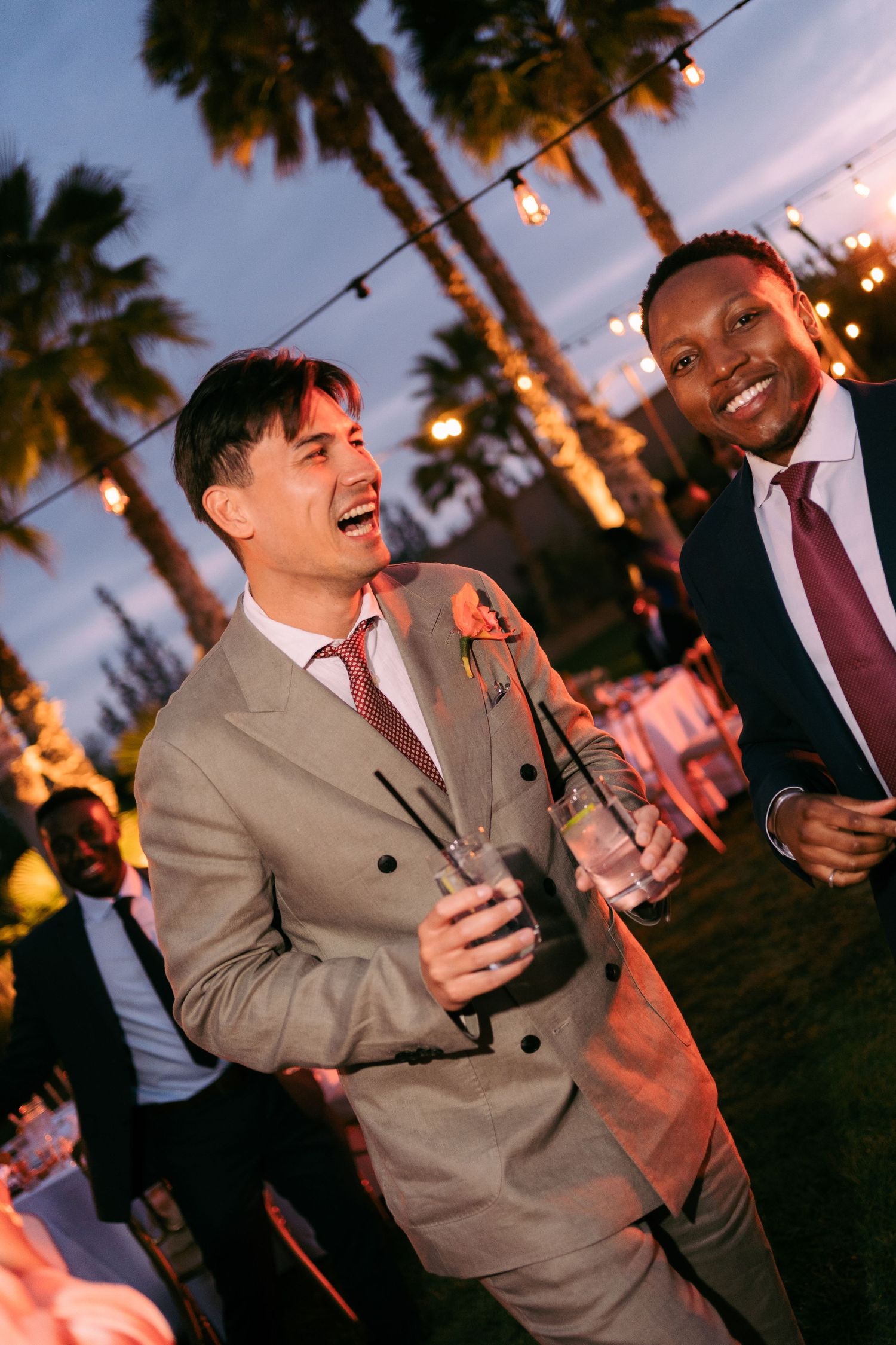 Group enjoying drinks and laughter at an outdoor evening party with string lights.
