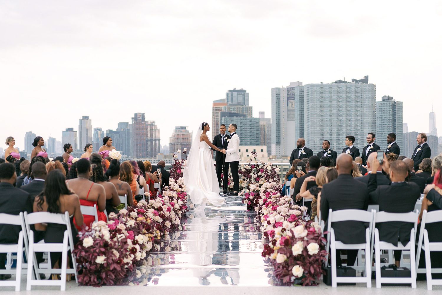 A rooftop wedding ceremony with pink and white floral aisle decorations against a cityscape backdrop.