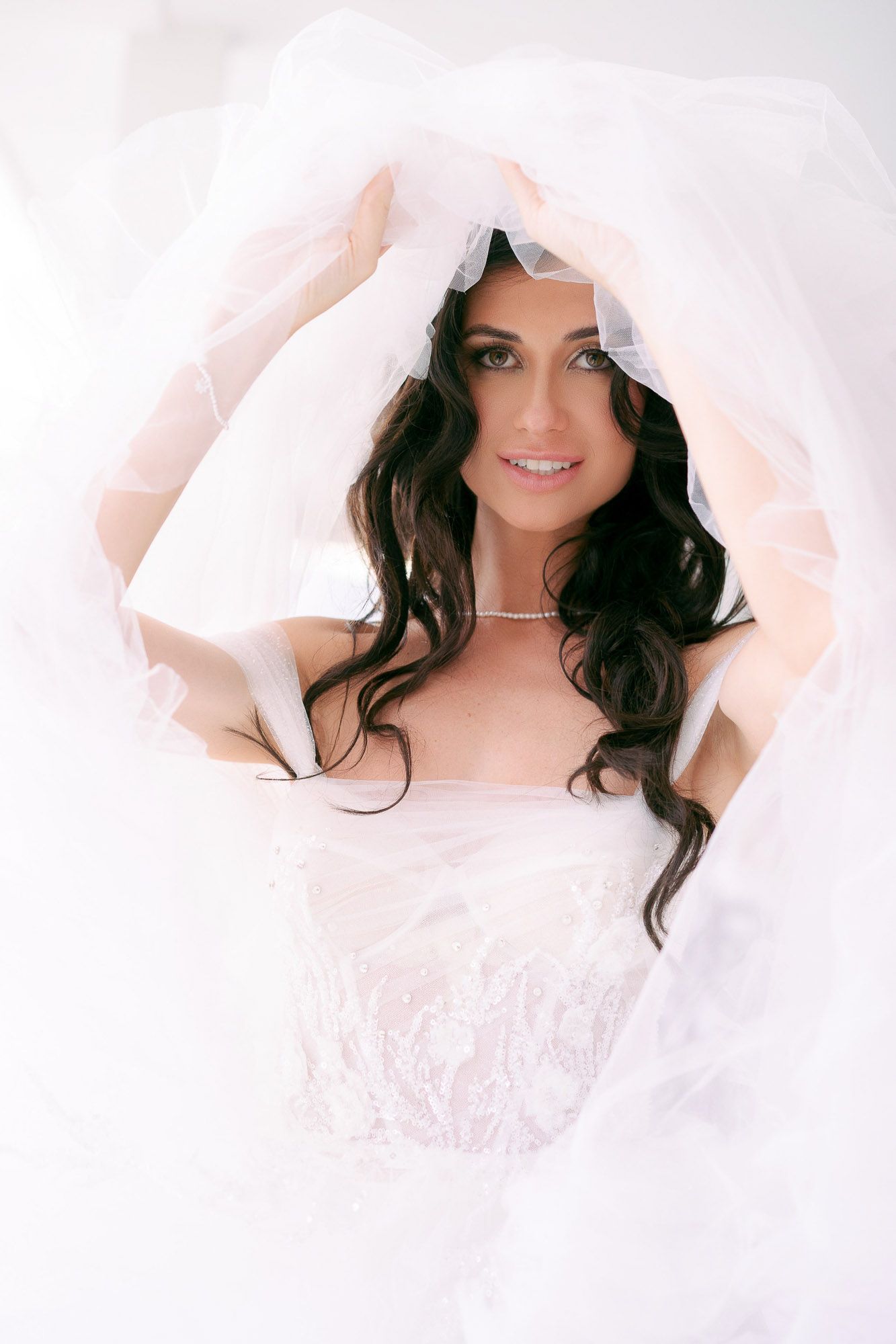 Ethereal bridal portrait series featuring soft white tulle fabric framing dark wavy hair against light background.