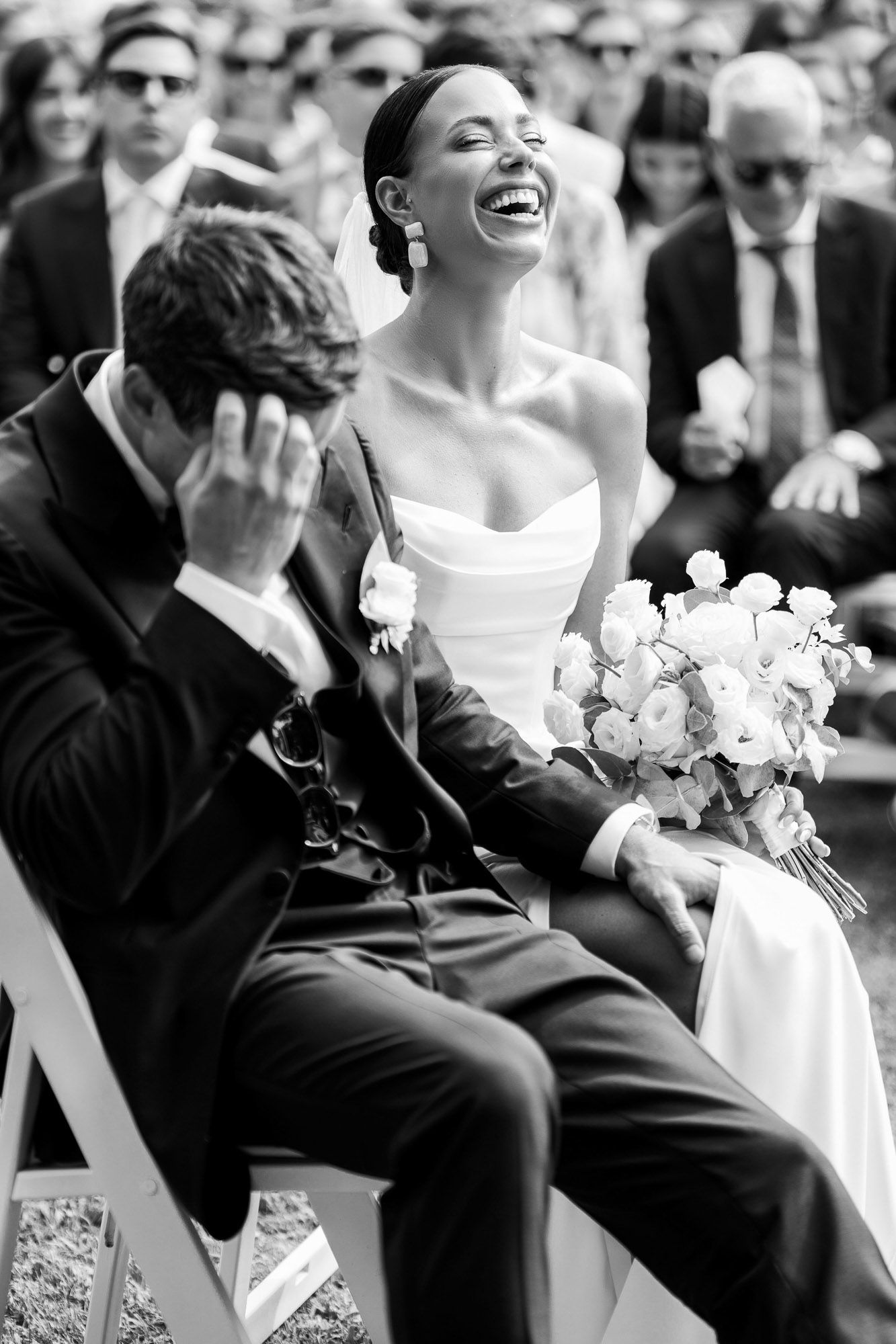 A candid black and white wedding photo capturing a joyful moment of laughter between a bride and groom during their ceremony.