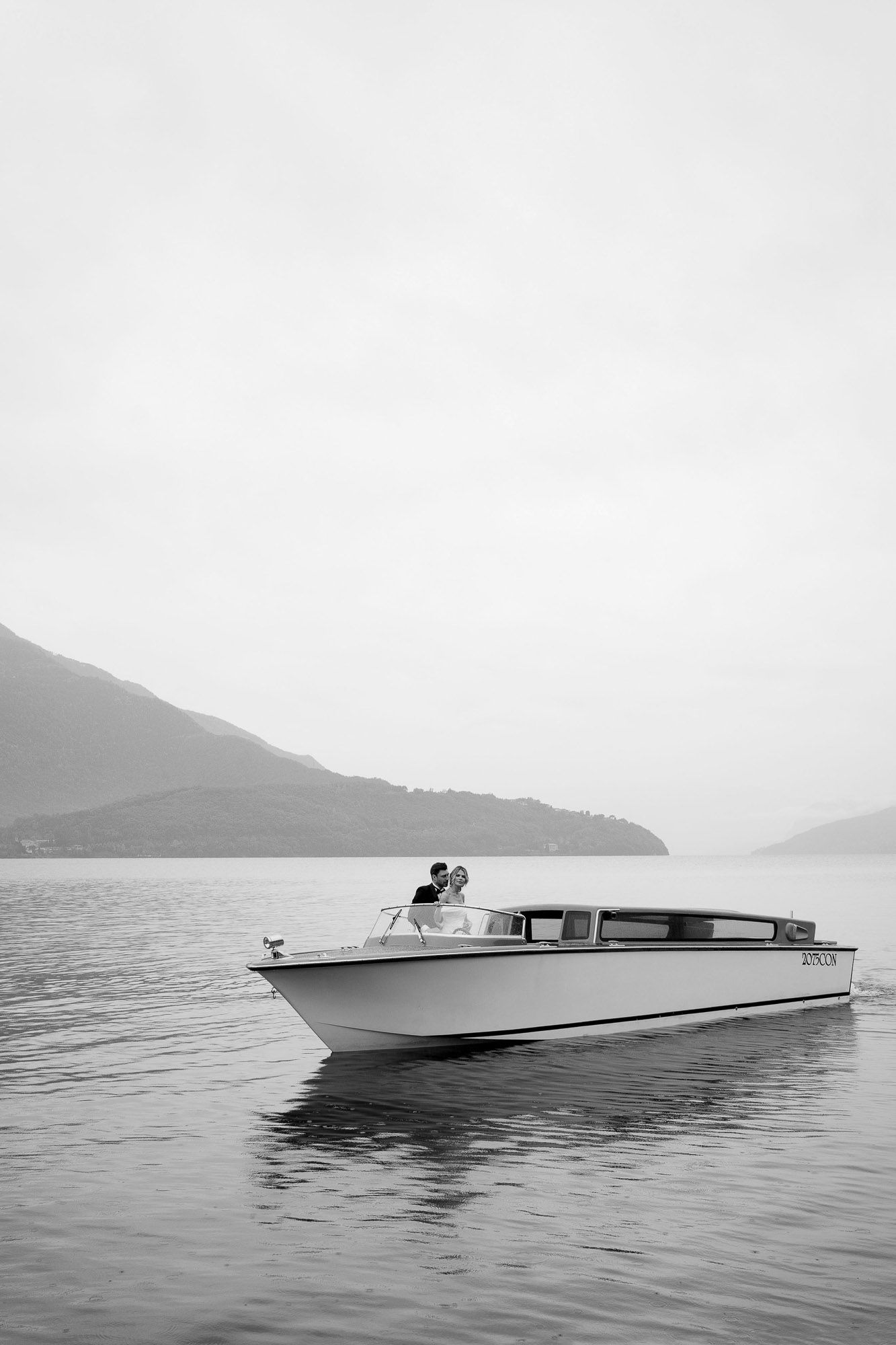 Vintage black and white photographs of a sleek wooden speedboat cruising across calm lake waters with mountains in background.