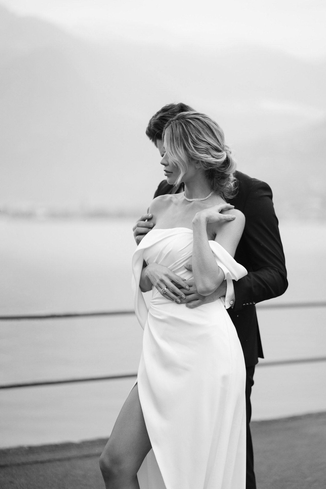 A romantic black and white photo of an intimate couple embracing outdoors, with a flowing white dress against dark attire.