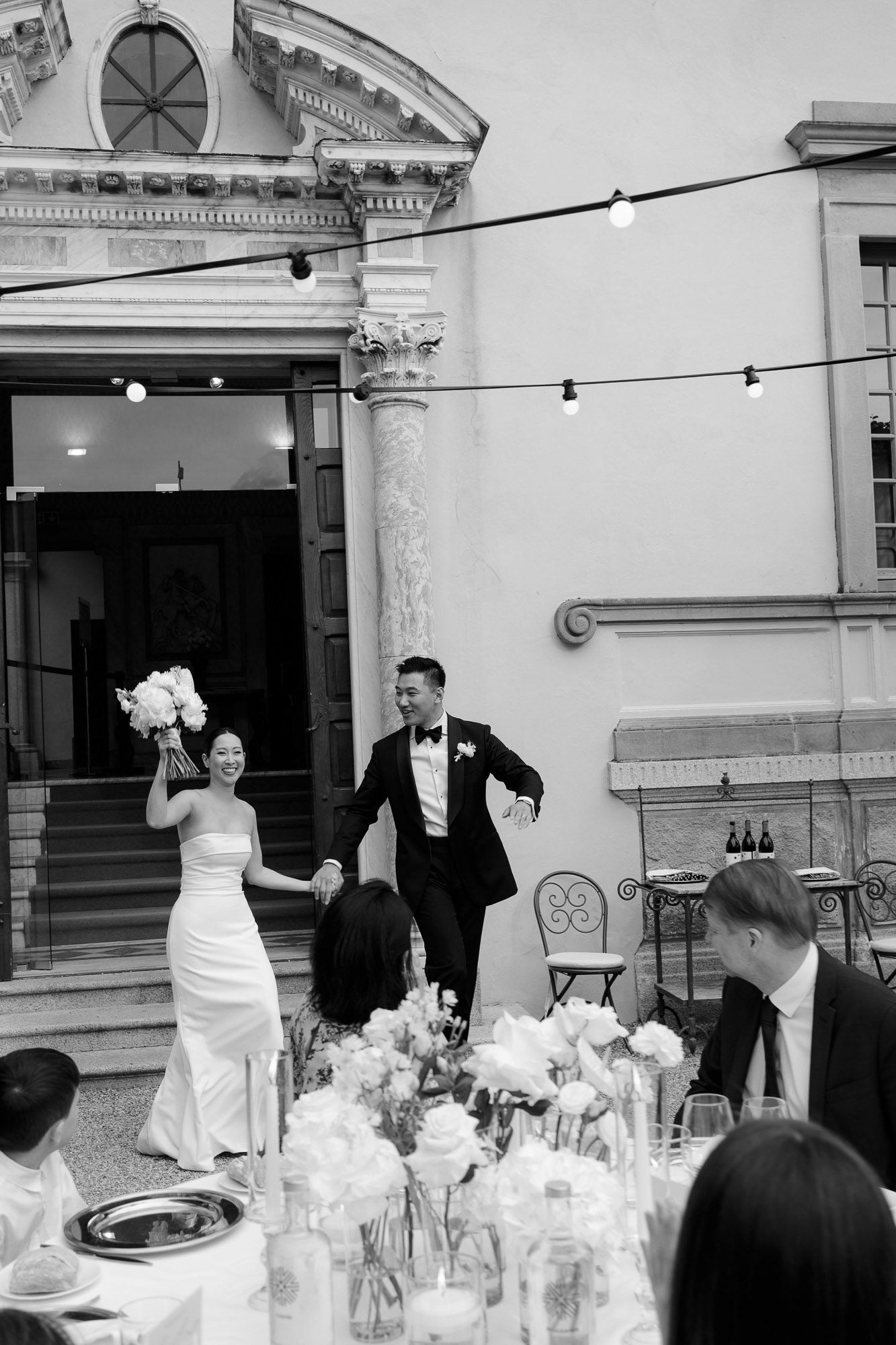 A black and white wedding reception scene with elegant table settings and string lights creating a romantic atmosphere.