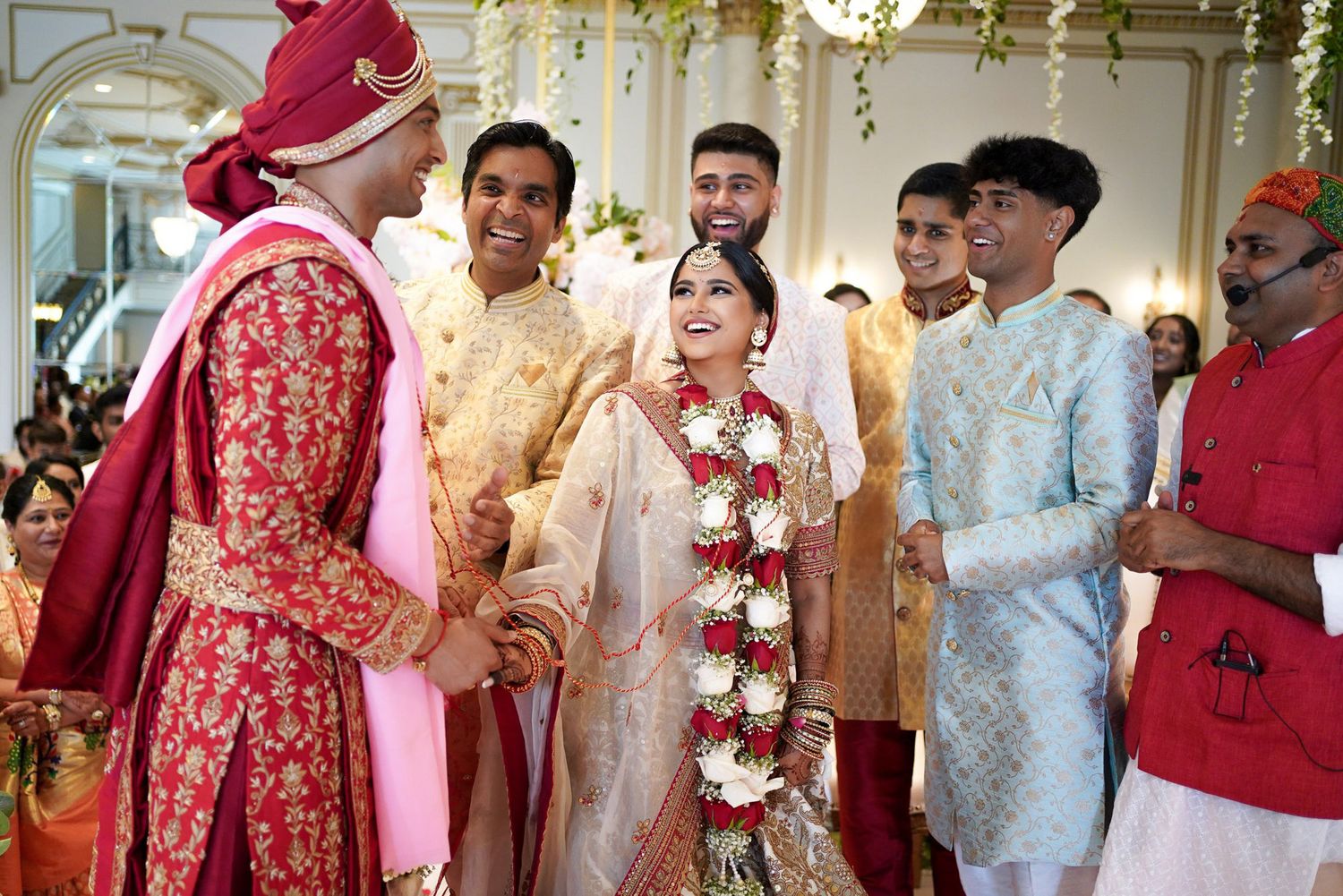Guests in traditional Indian wedding attire celebrate during a festive ceremony with red and white floral decorations.