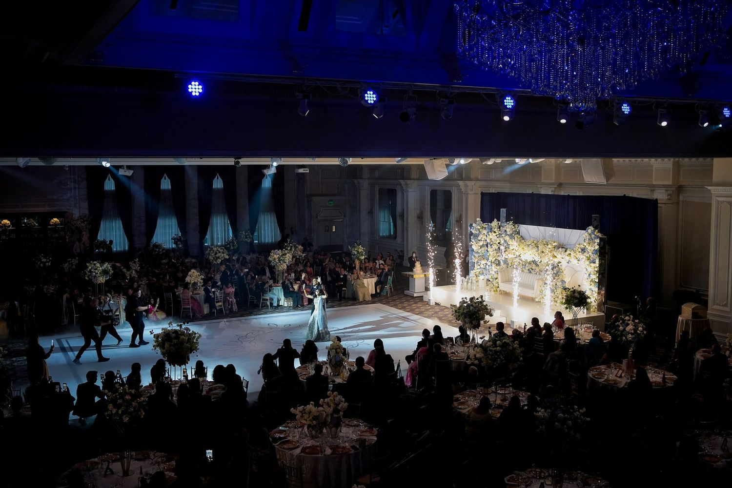 Dimly lit banquet hall with blue lighting and multiple round tables set up for an elegant evening event.