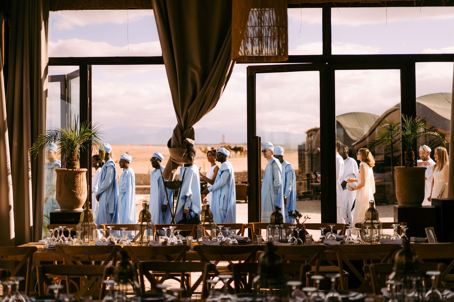 Wedding ceremony and reception venue with elegant drapery and large windows overlooking scenic landscape at sunset.