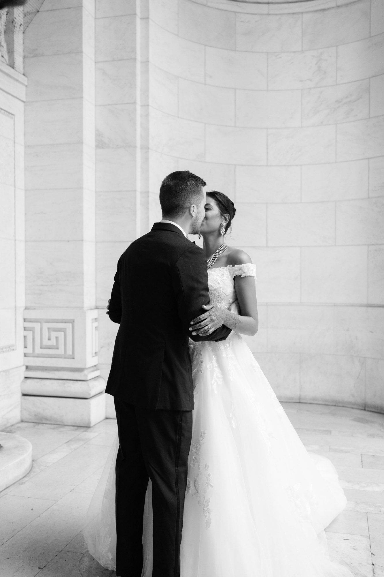 Black and white wedding photo series showing intimate moments between a bride and groom in an elegant marble hallway.