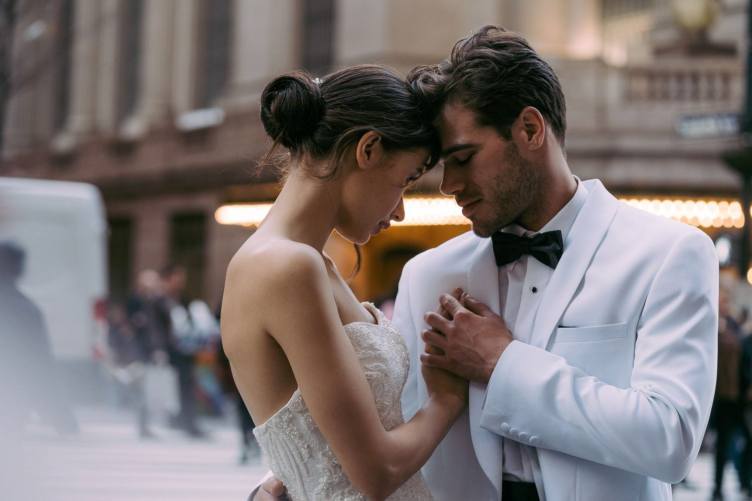 A romantic couple in formal wedding attire share an intimate dance moment on a city street at dusk.