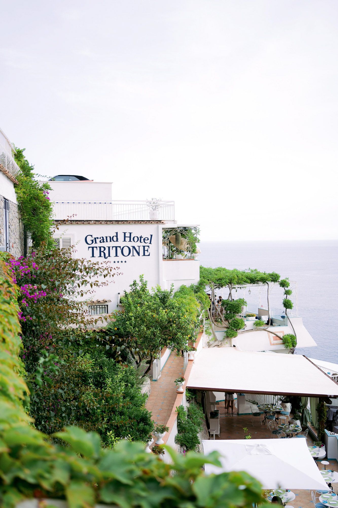 Exterior view of Grand Hotel Tritone nestled on a hillside with lush greenery and white architecture.