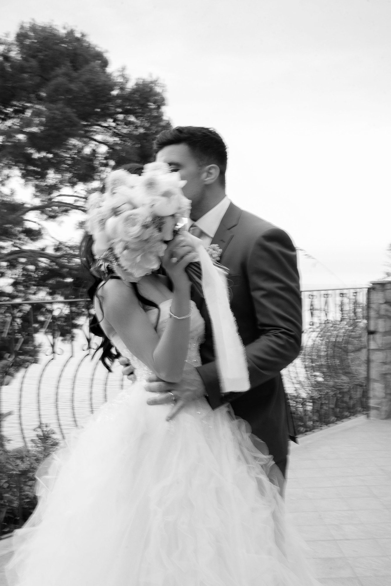 A romantic black and white photo series showing a bride and groom sharing intimate kisses in an outdoor setting.