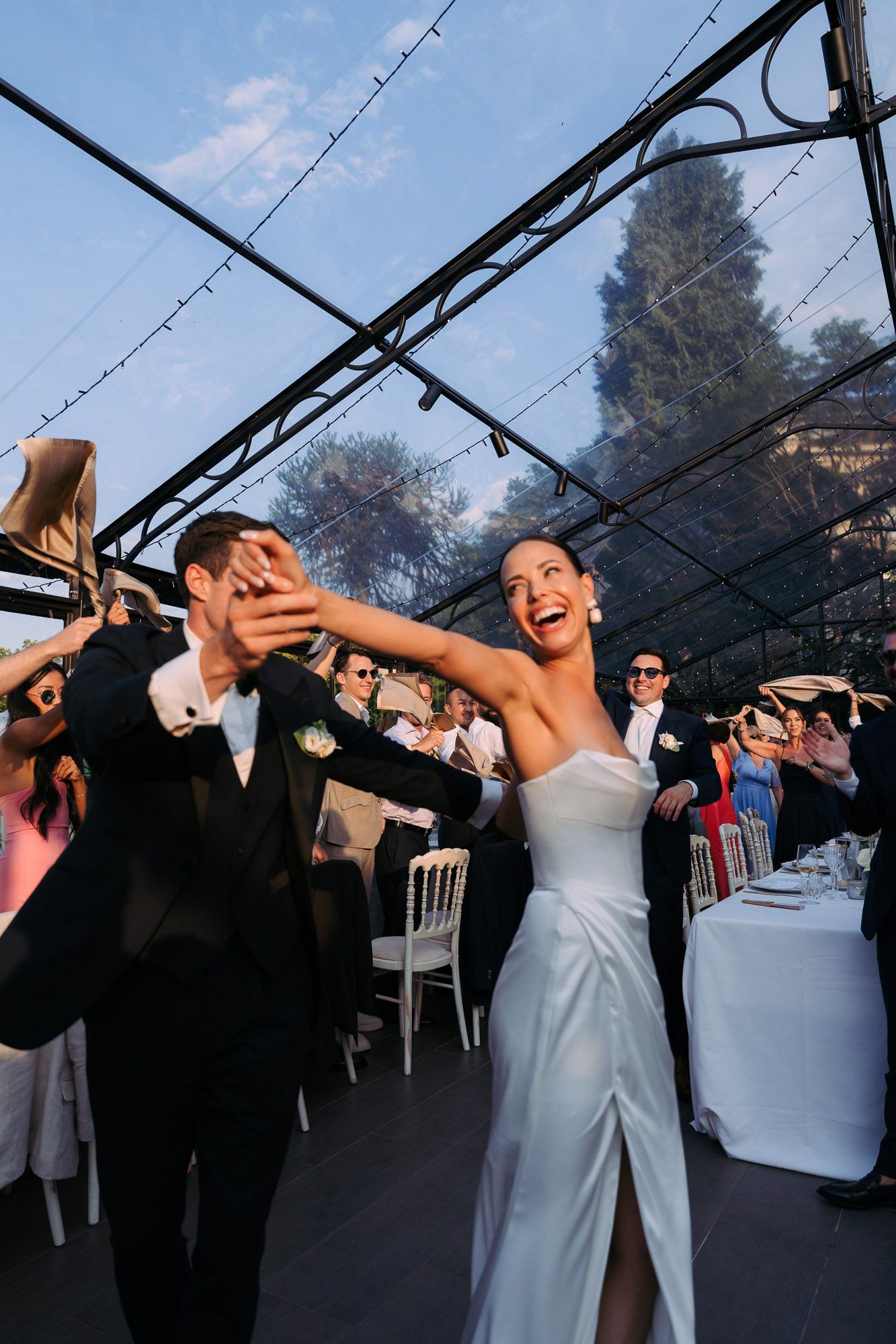 A couple shares a joyful dance moment under a tented reception venue with string lights overhead.