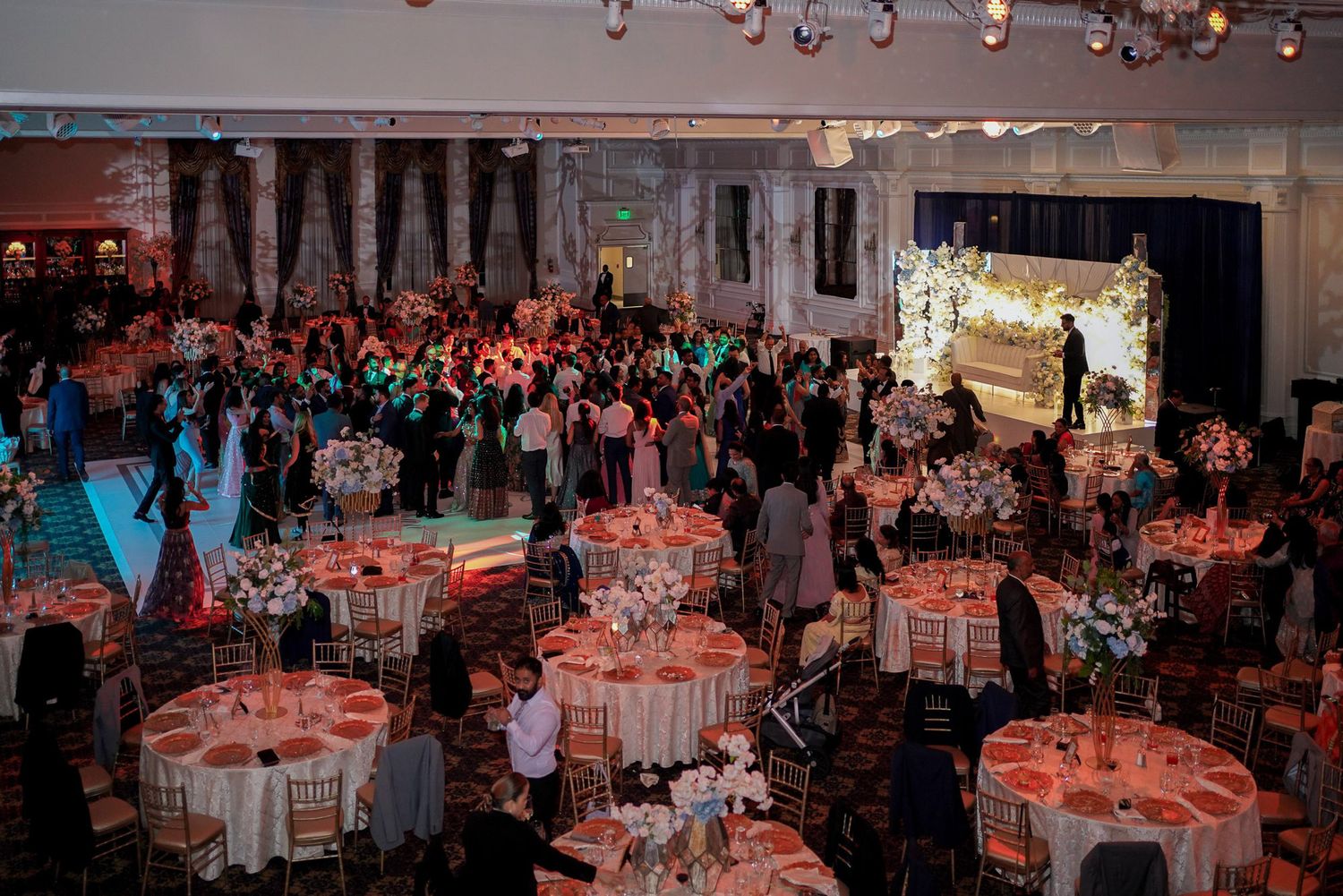Large ballroom decorated with round tables and red accent lighting for a formal dinner reception.