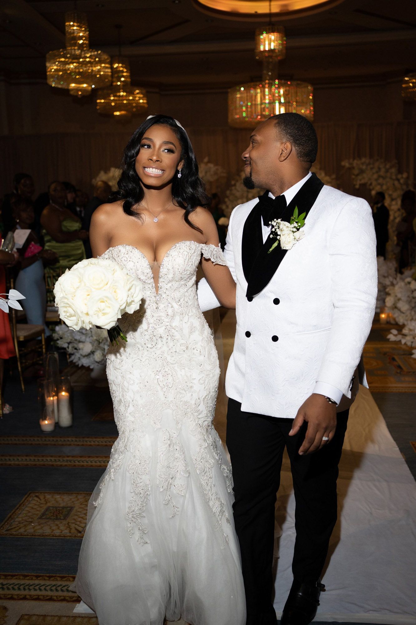 A couple shares a joyful moment during their wedding reception in an elegant ballroom with chandeliers.