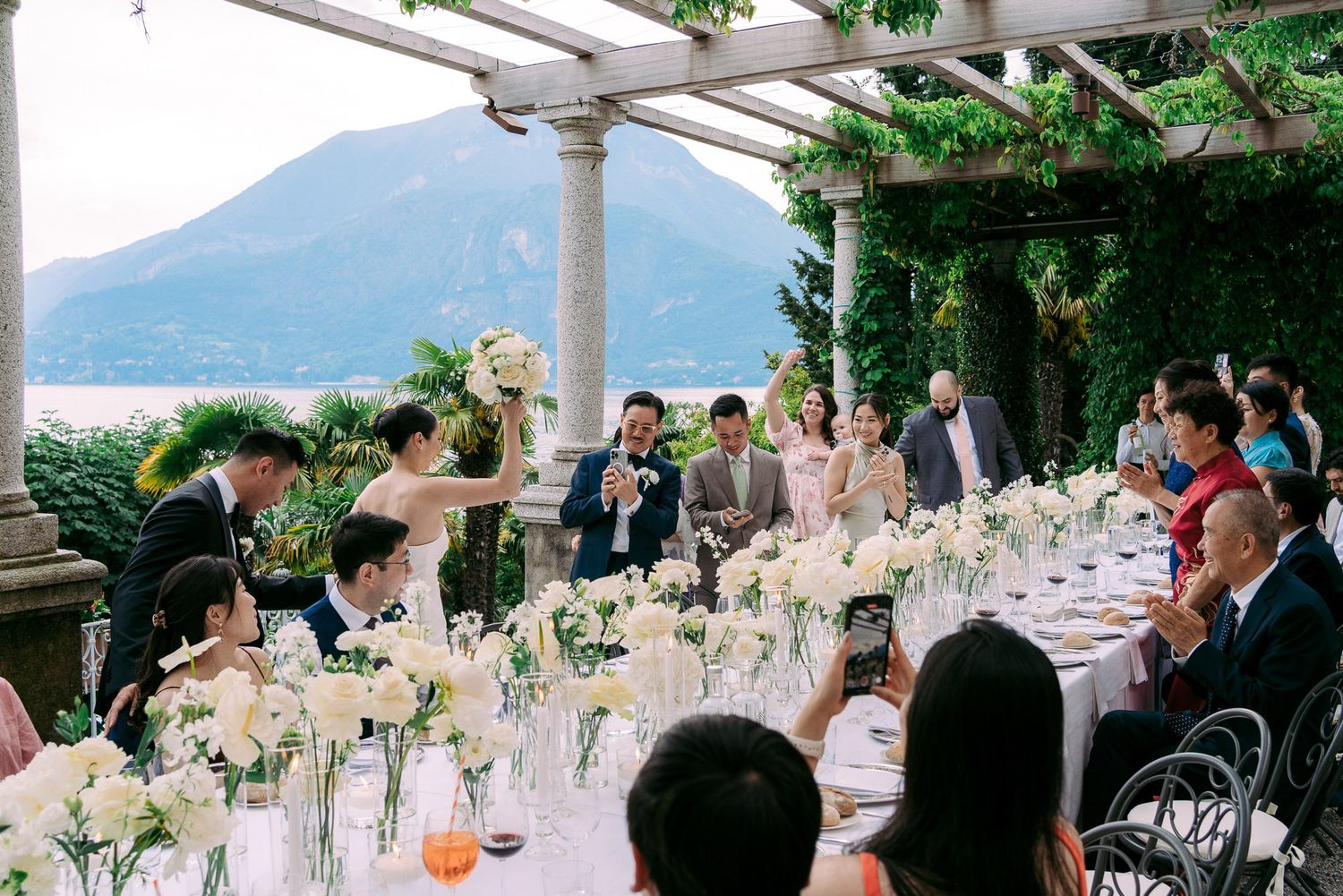 Wedding reception guests seated at elegant tables with mountain views and floral centerpieces at an outdoor venue.