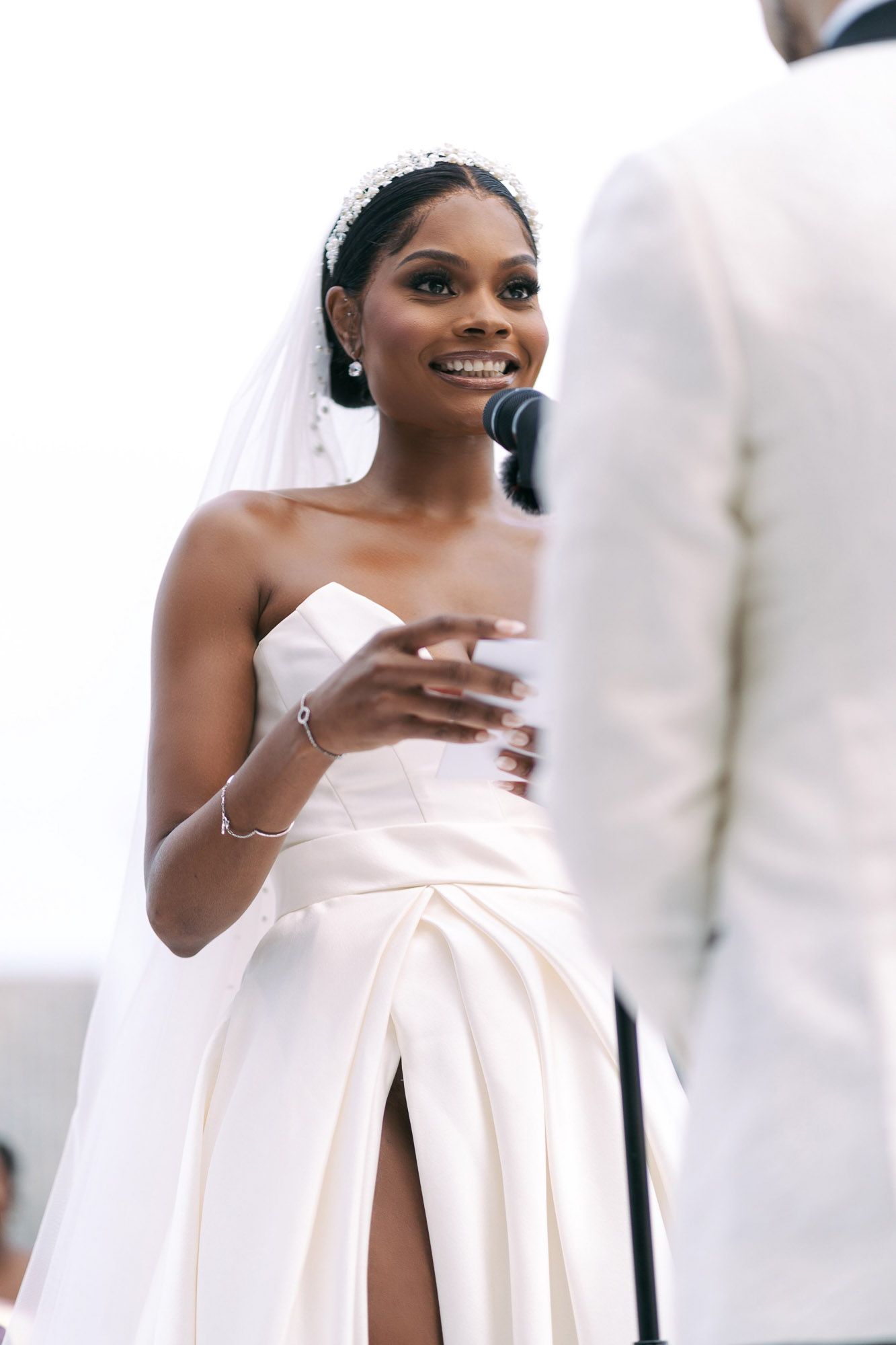 Bride in a white strapless wedding dress smiles while holding a glass during a celebration.