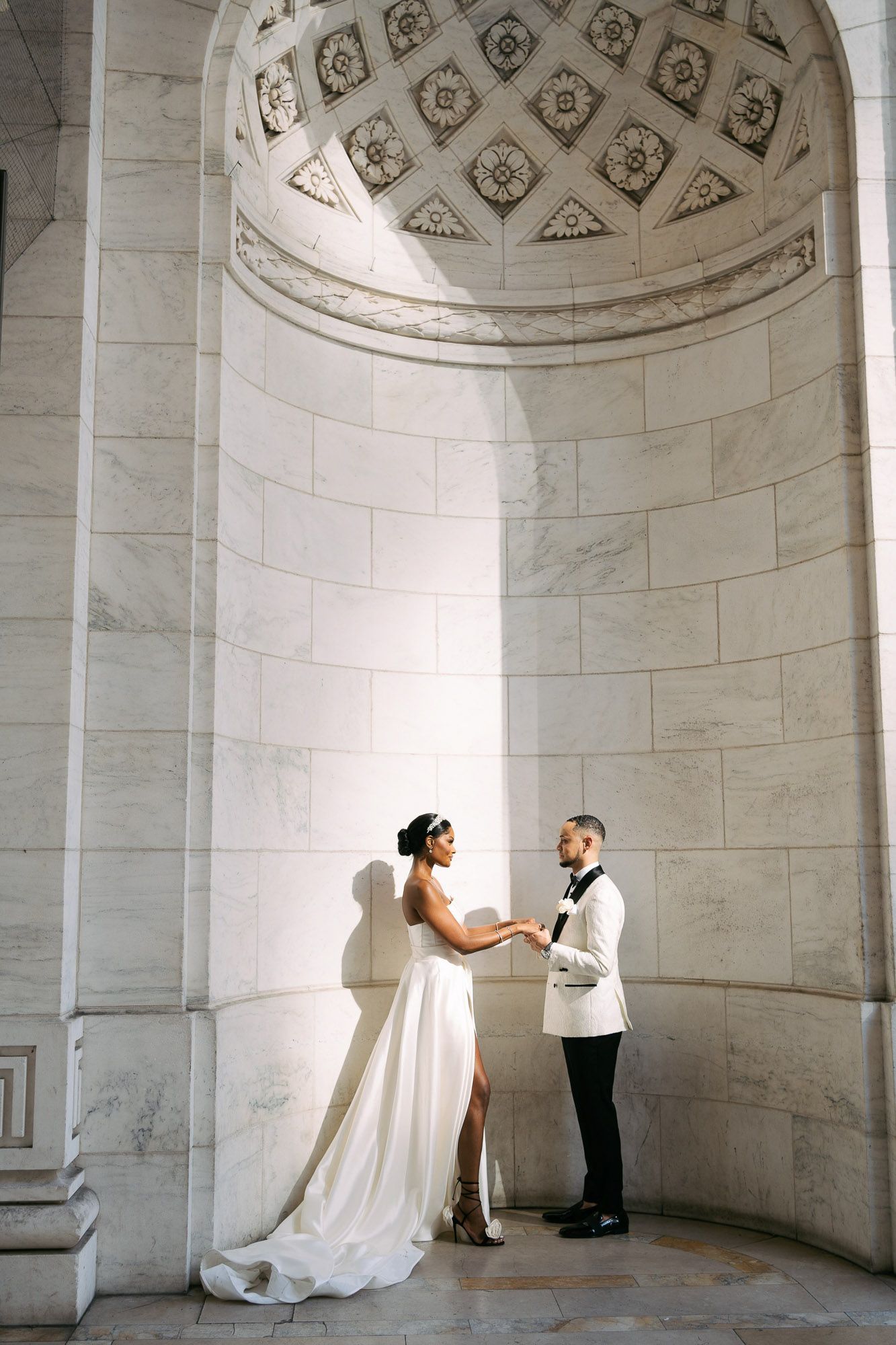 Bride and groom share a moment under ornate domed architecture in an elegant white wedding setting.