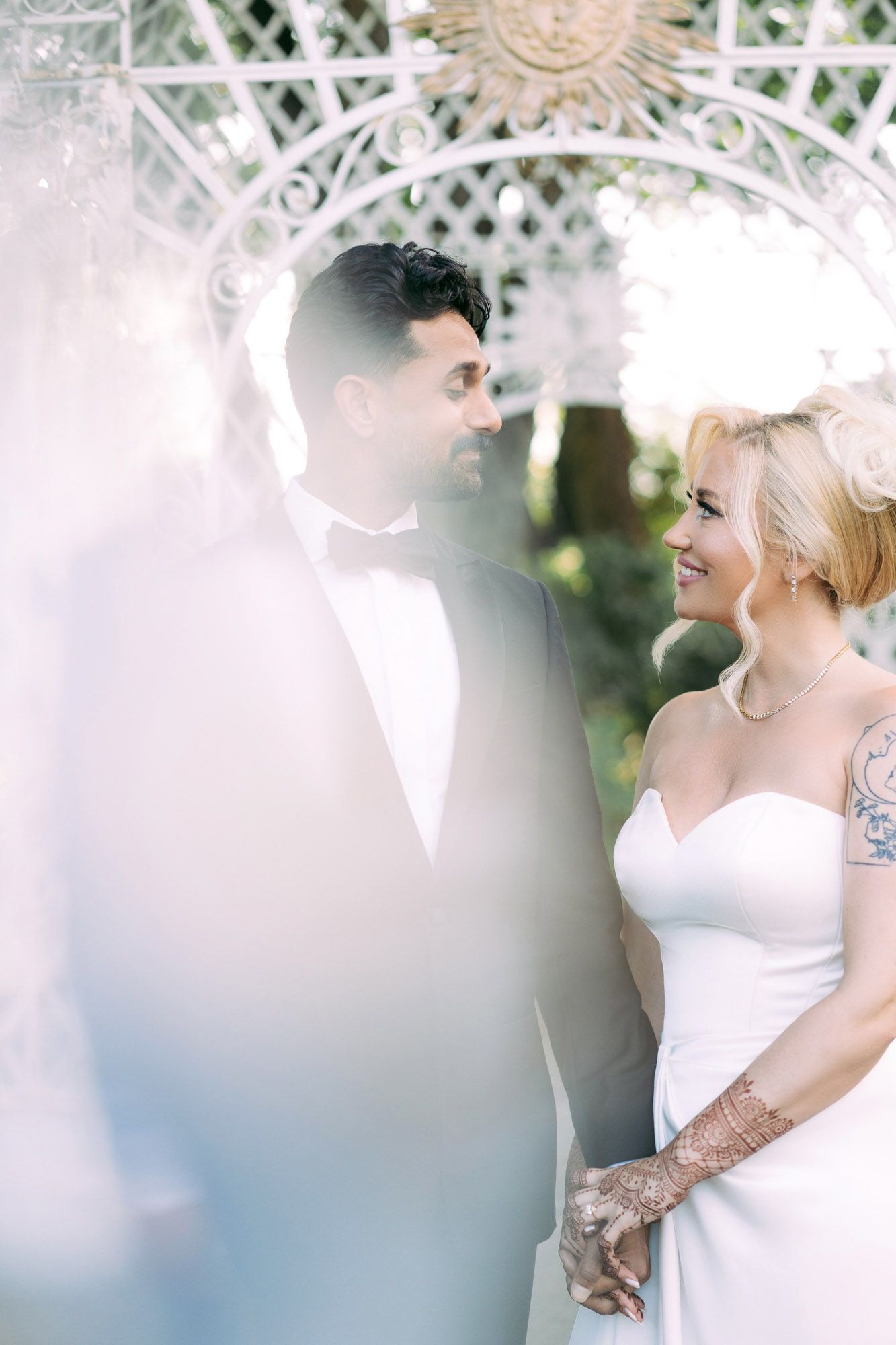 A romantic wedding moment captured under a white lattice arch with soft dreamy lighting effects.