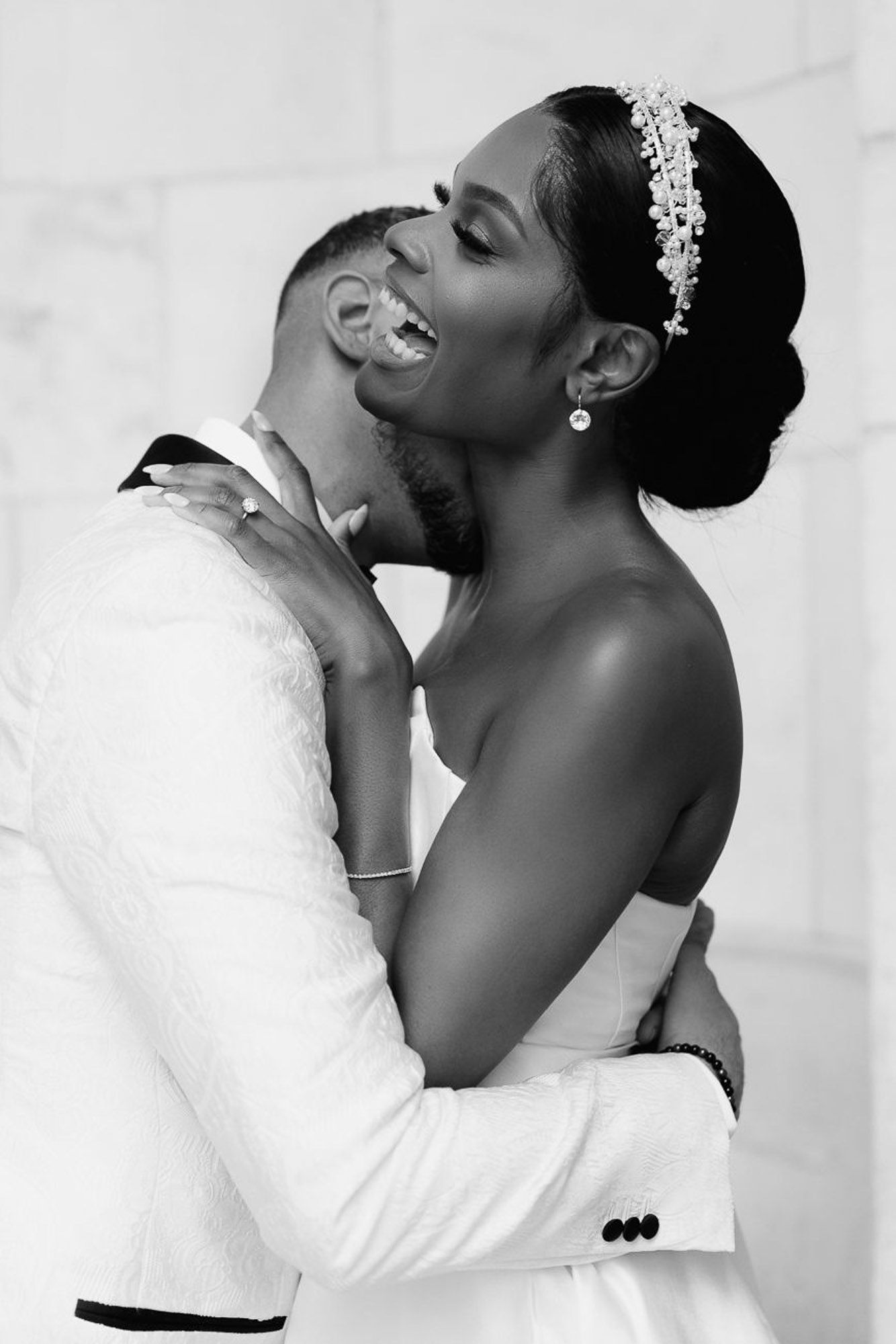 A romantic black and white wedding portrait shows a tender embrace between newlyweds in elegant attire.