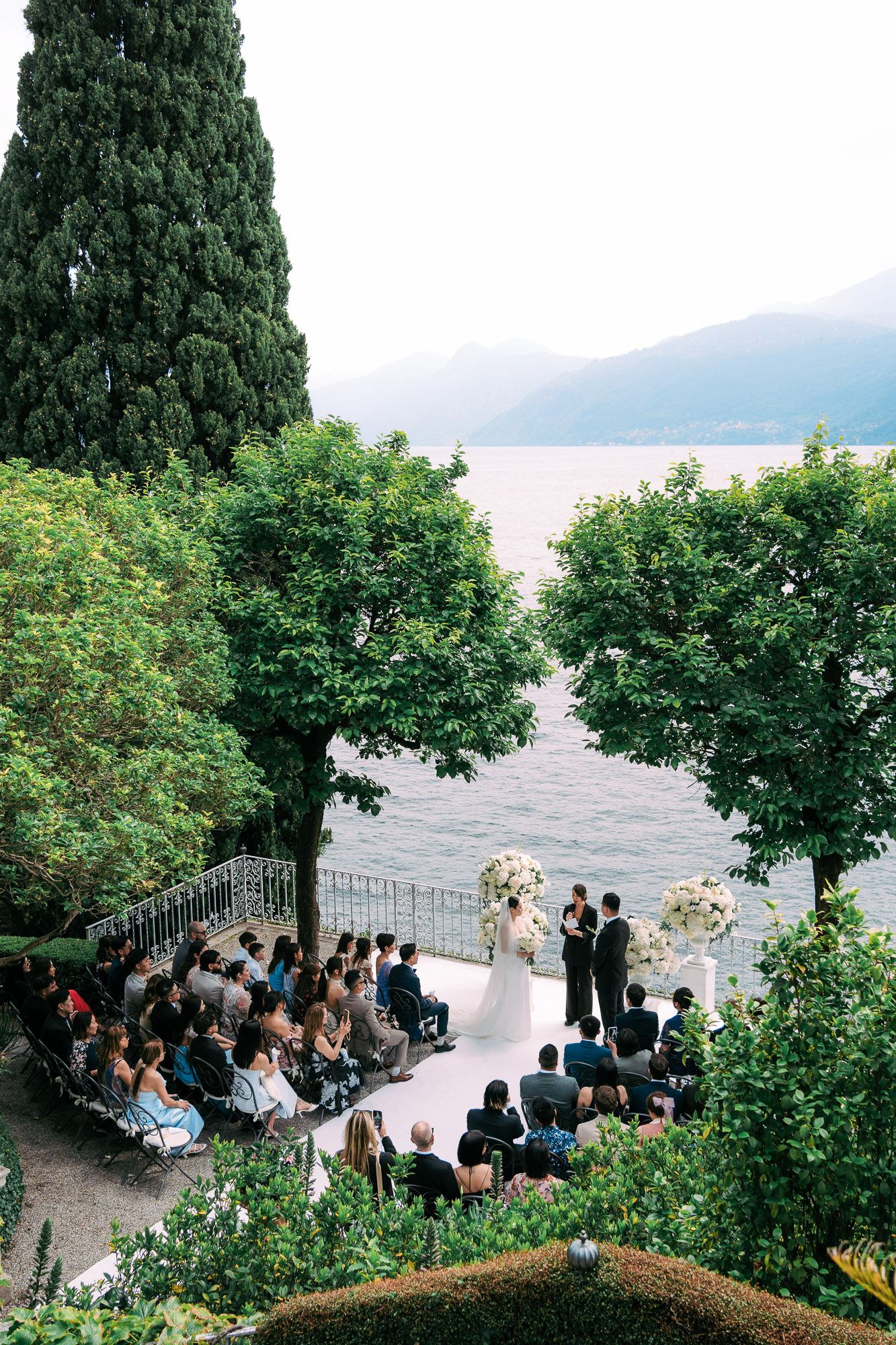 Intimate outdoor wedding ceremony set against a backdrop of cypress trees and a tranquil lake view.
