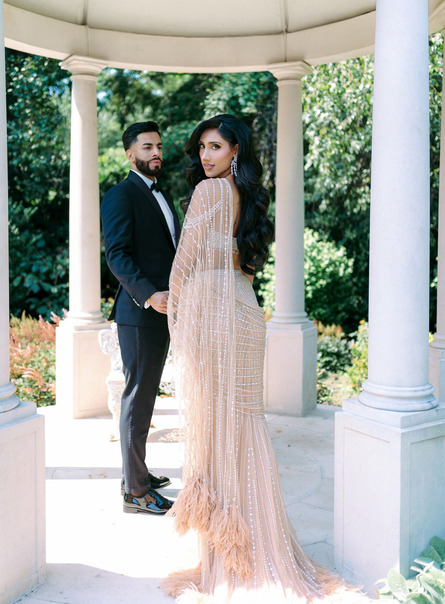 Couple sharing a romantic moment in an elegant white gazebo surrounded by lush greenery and gardens.