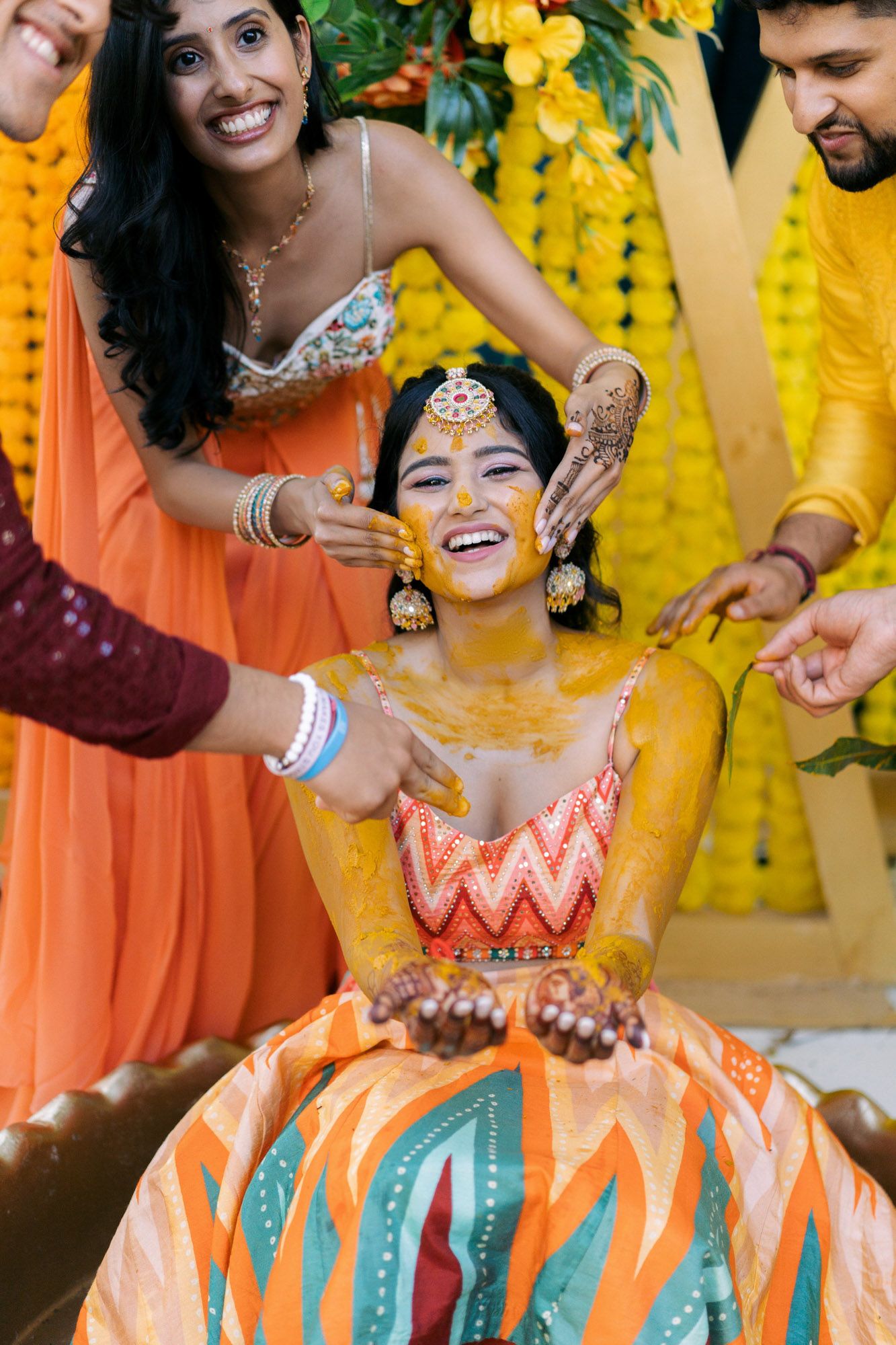 Traditional Haldi ceremony with turmeric being applied during an Indian wedding celebration against yellow backdrop.