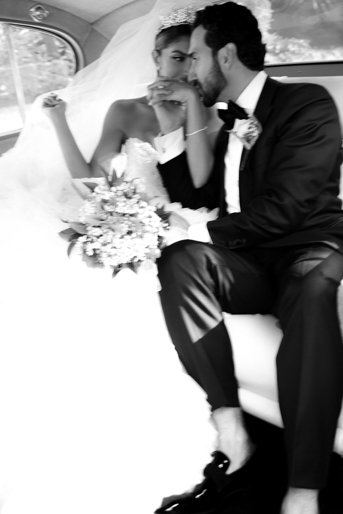 A romantic black and white wedding photo of newlyweds sharing an intimate moment in the back of a car.