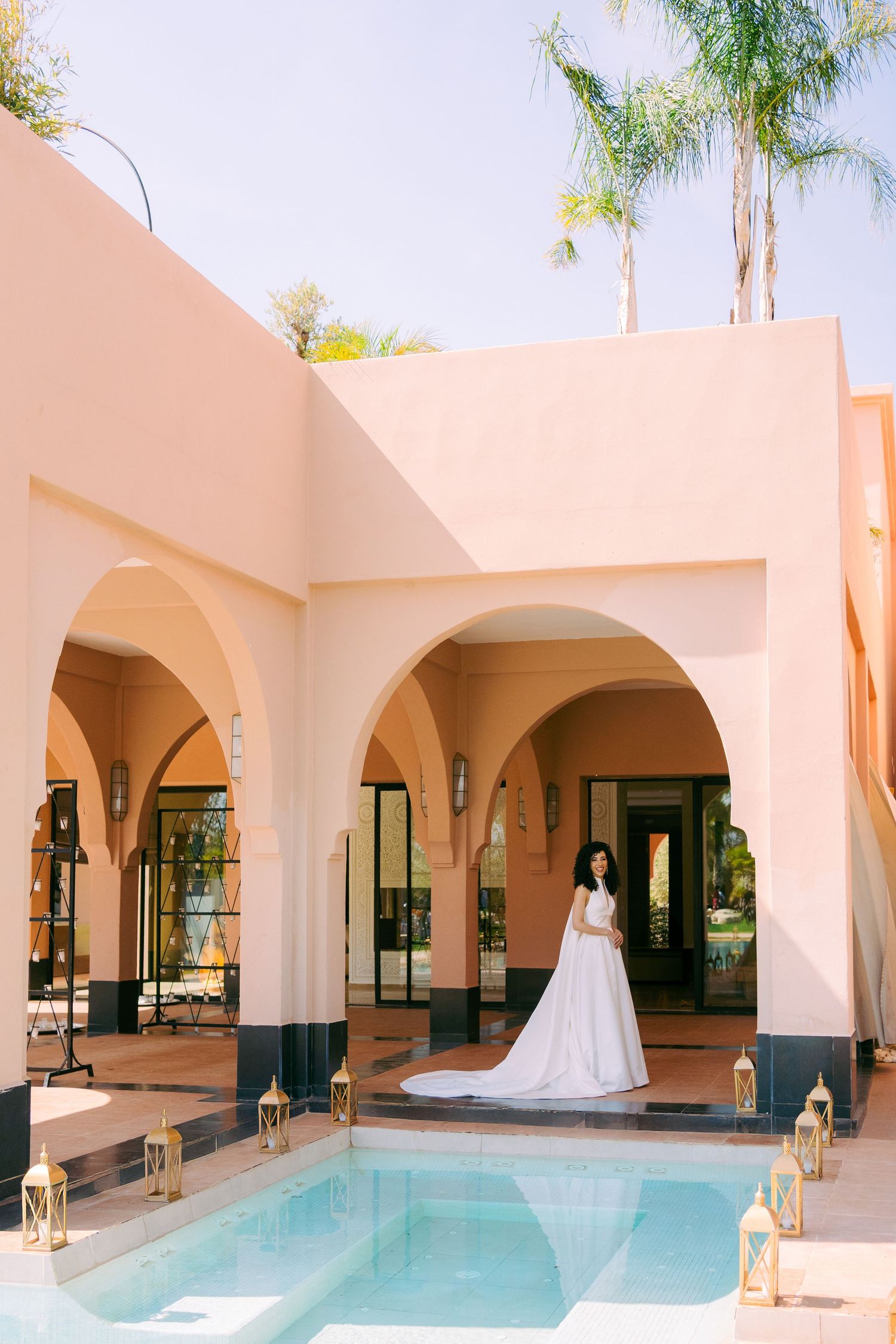 Modern courtyard with arched walkways and a long swimming pool surrounded by pink stucco walls.