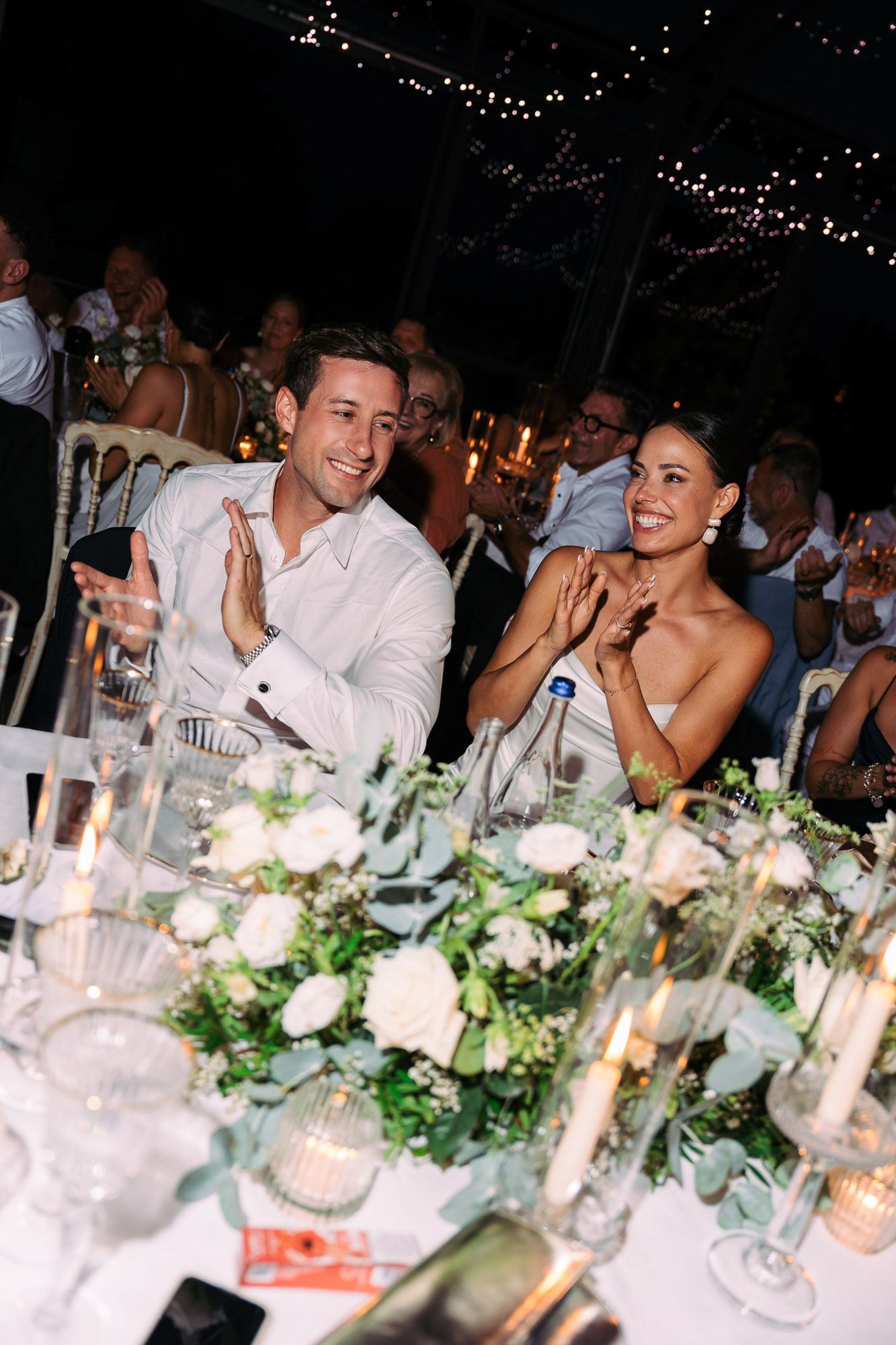 Wedding reception table decorated with white floral arrangements and glowing candles at an elegant evening celebration.