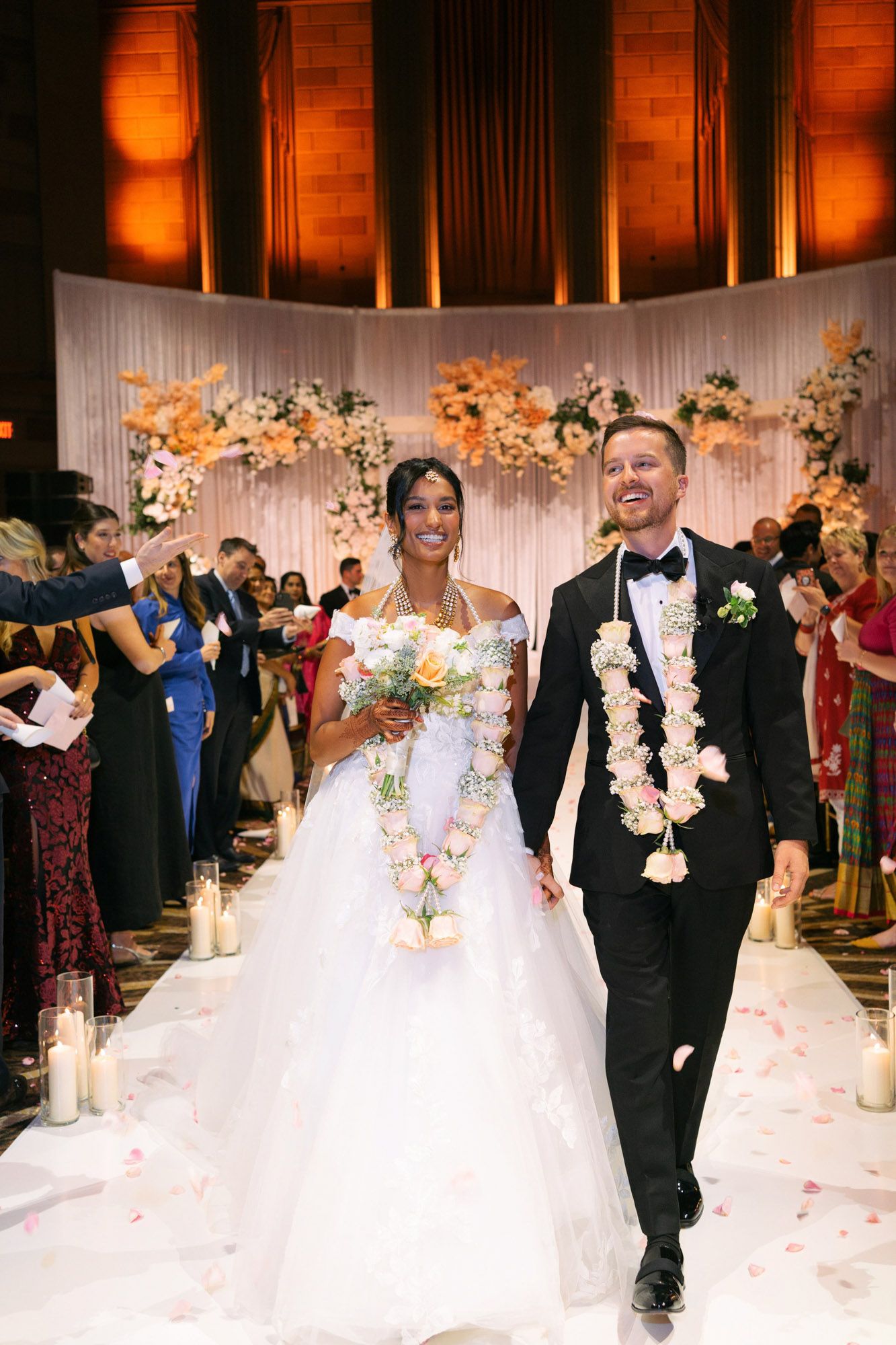 Newlyweds walk down the aisle at their wedding ceremony surrounded by floral decorations and guests.